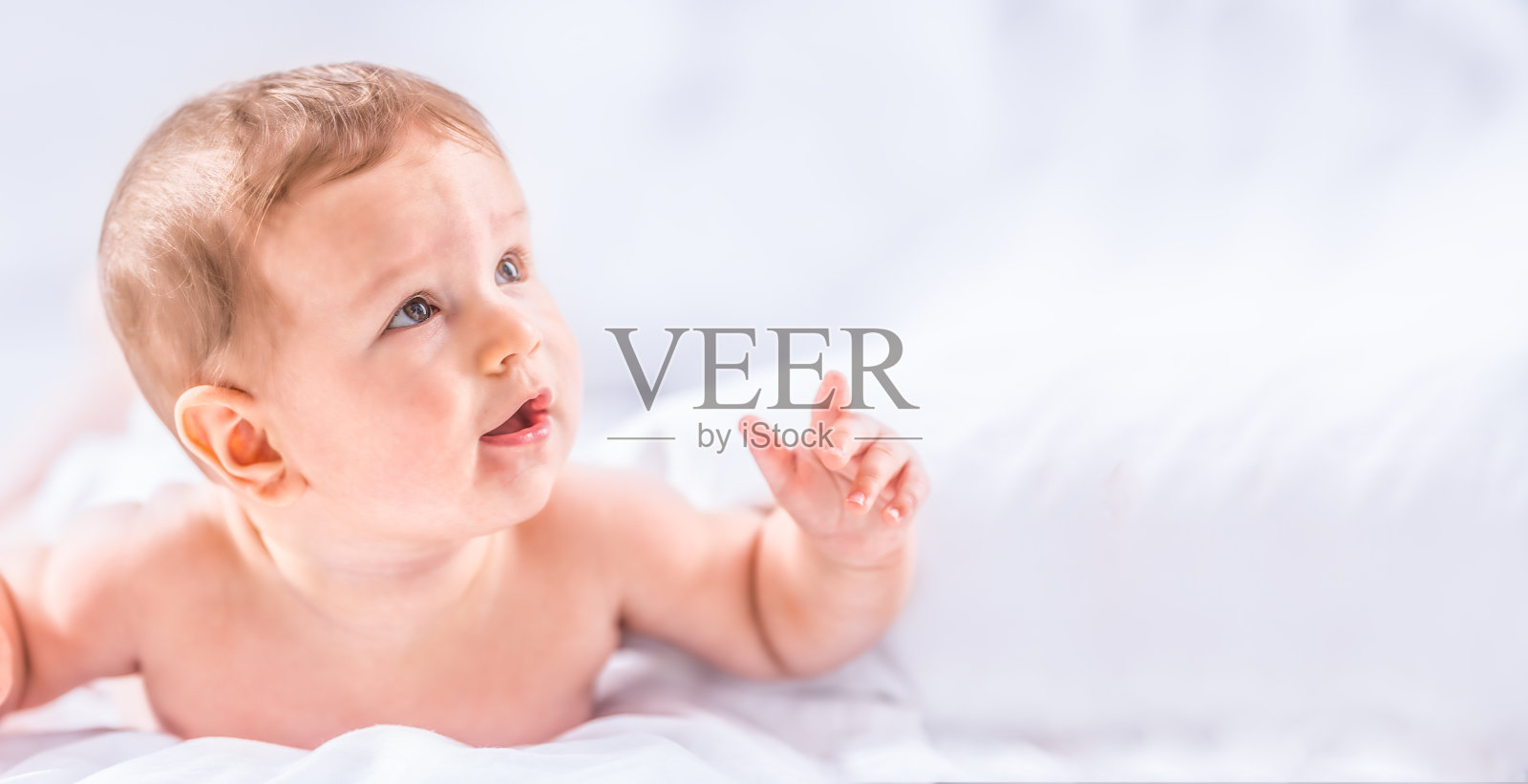 可爱的小男孩躺在床上的肖像。刚出生的孩子在卧室。婴儿俯卧着，抬起头。照片摄影图片