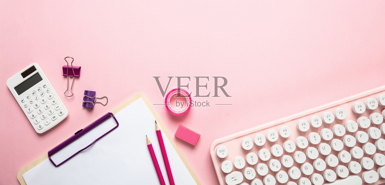 粉红色背景下的电脑键盘和办公用品照片摄影图片