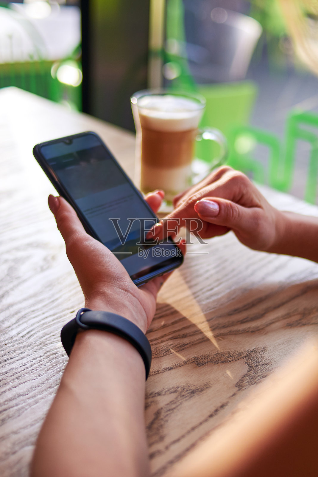 一位女士正拿着一杯卡布奇诺坐着，正在使用智能手机。照片摄影图片