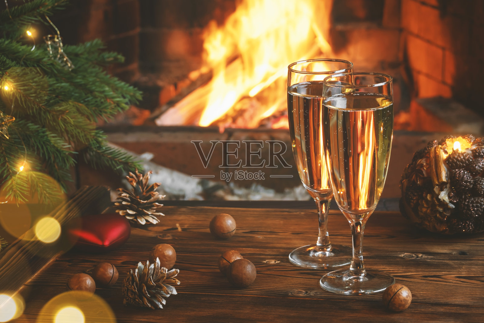 圣诞作文-在一个燃烧着壁炉的房间里，靠近圣诞树的木桌上放着两个装有香槟的杯子照片摄影图片