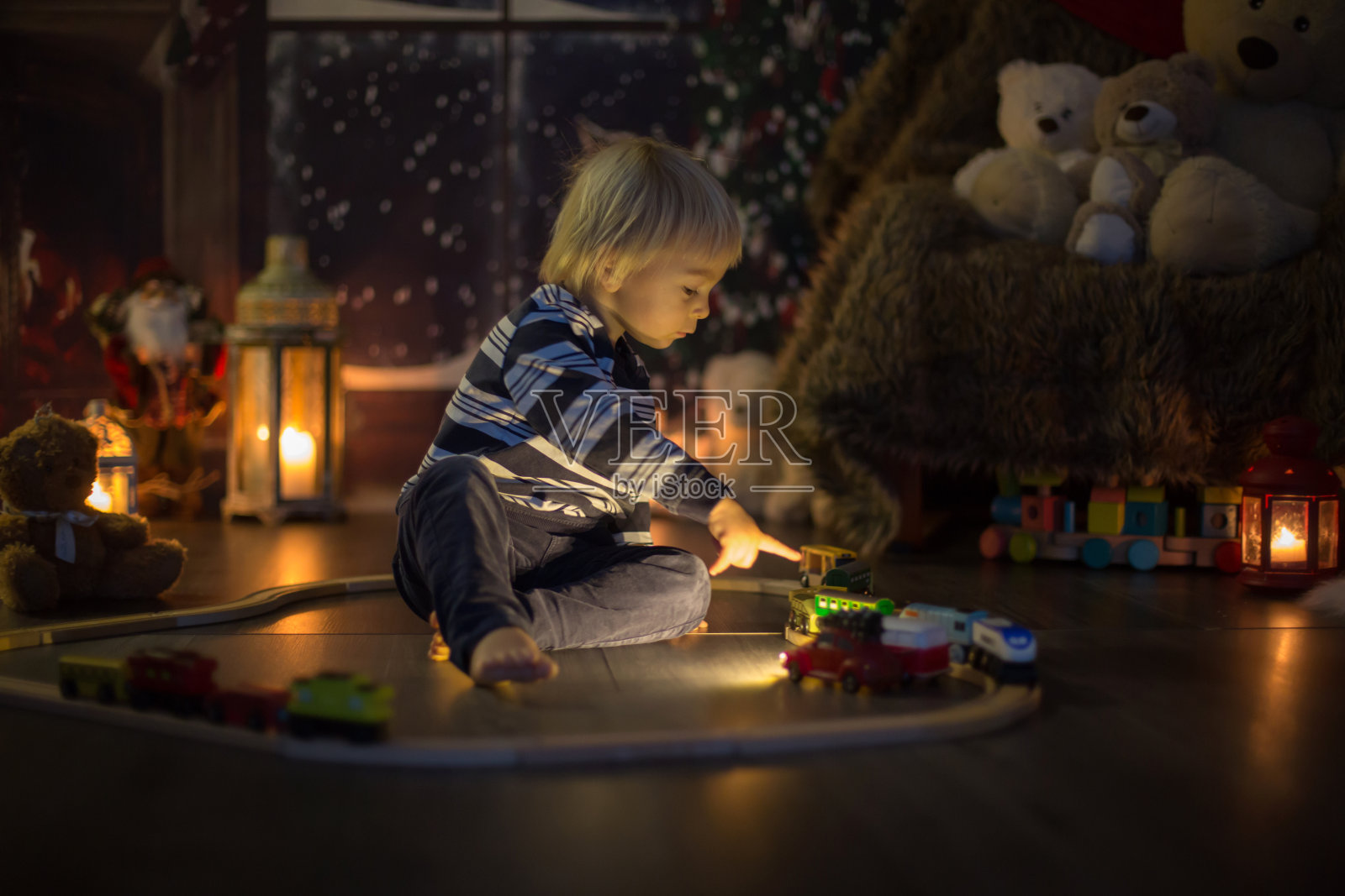 可爱的蹒跚学步的小男孩，圣诞节晚上在家玩木火车照片摄影图片