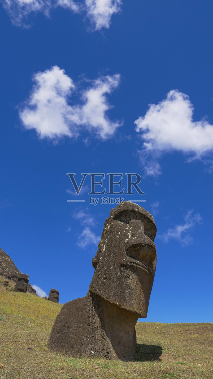 垂直方向:白云漂浮在遥远的异国小岛上的两个巨大的摩埃石像之上。照片摄影图片