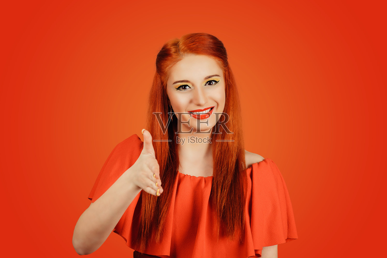 肖像特写的一个红头发的女人在一个红色的裙子伸出她的手会见某人，给一个孤立的握手在一个红色的背景。照片摄影图片