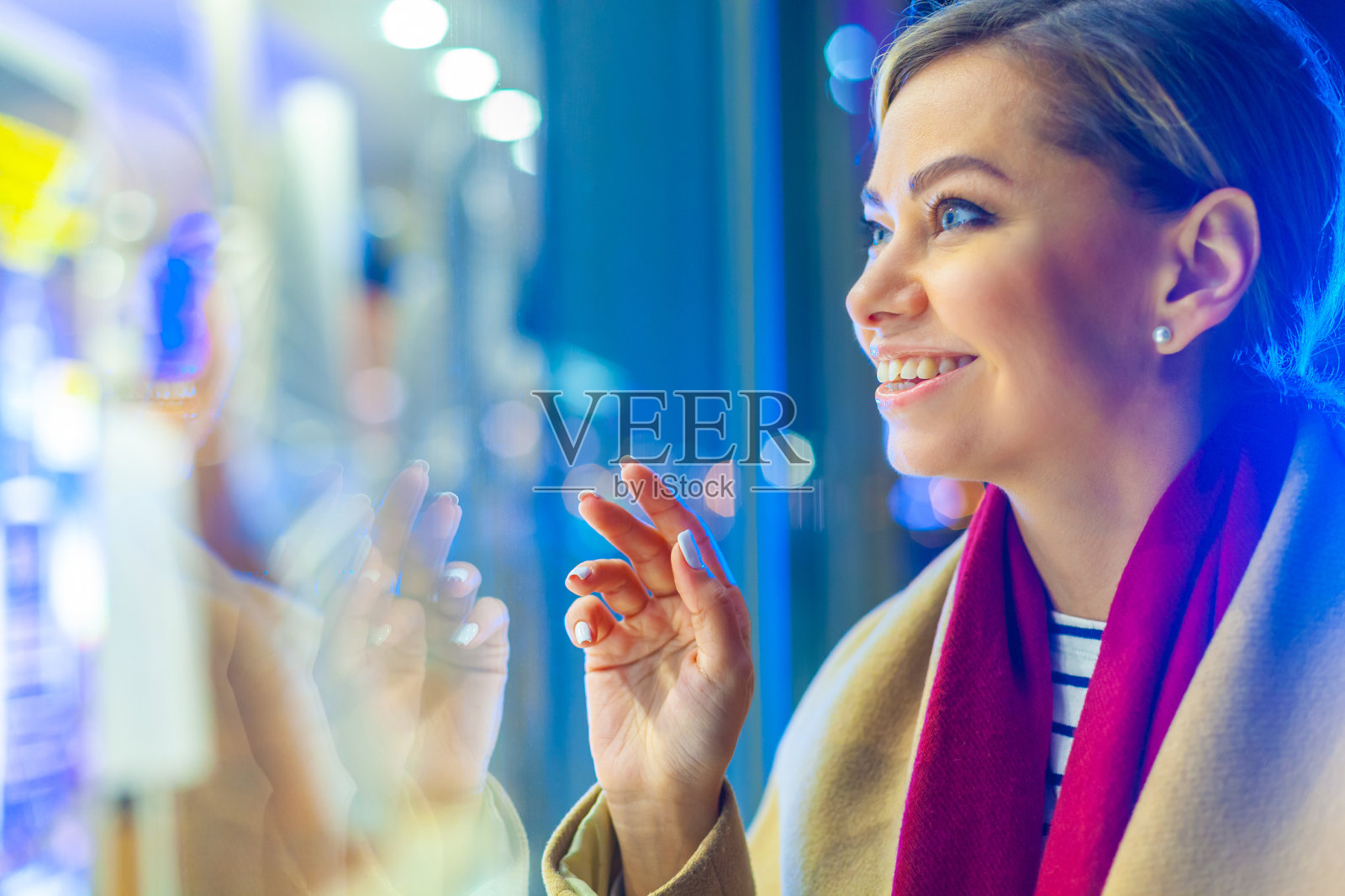 圣诞节。一个年轻美丽的女人在深夜看着发光的窗户，选择了一份礼物。多彩的，神奇的灯光，美丽的眩光。快乐的女孩望着窗外，痛苦的选择照片摄影图片