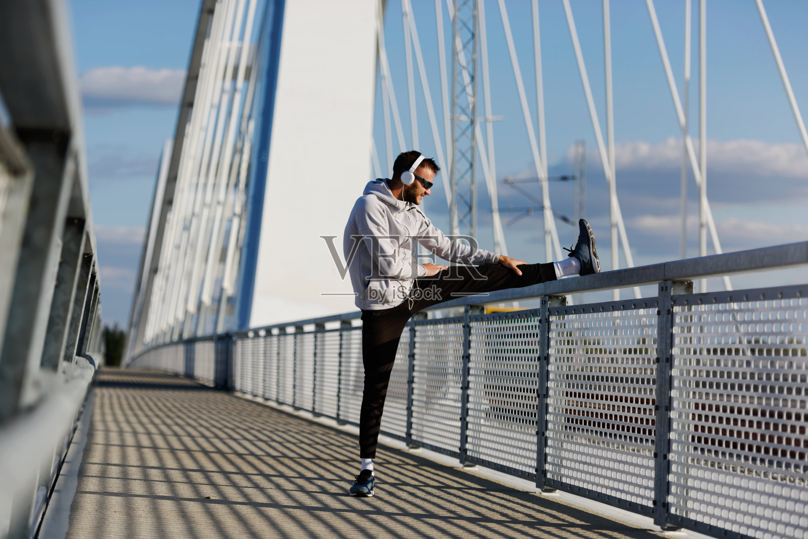 在阳光明媚的日子里，年轻的运动员在桥上跑步前伸展肌肉照片摄影图片