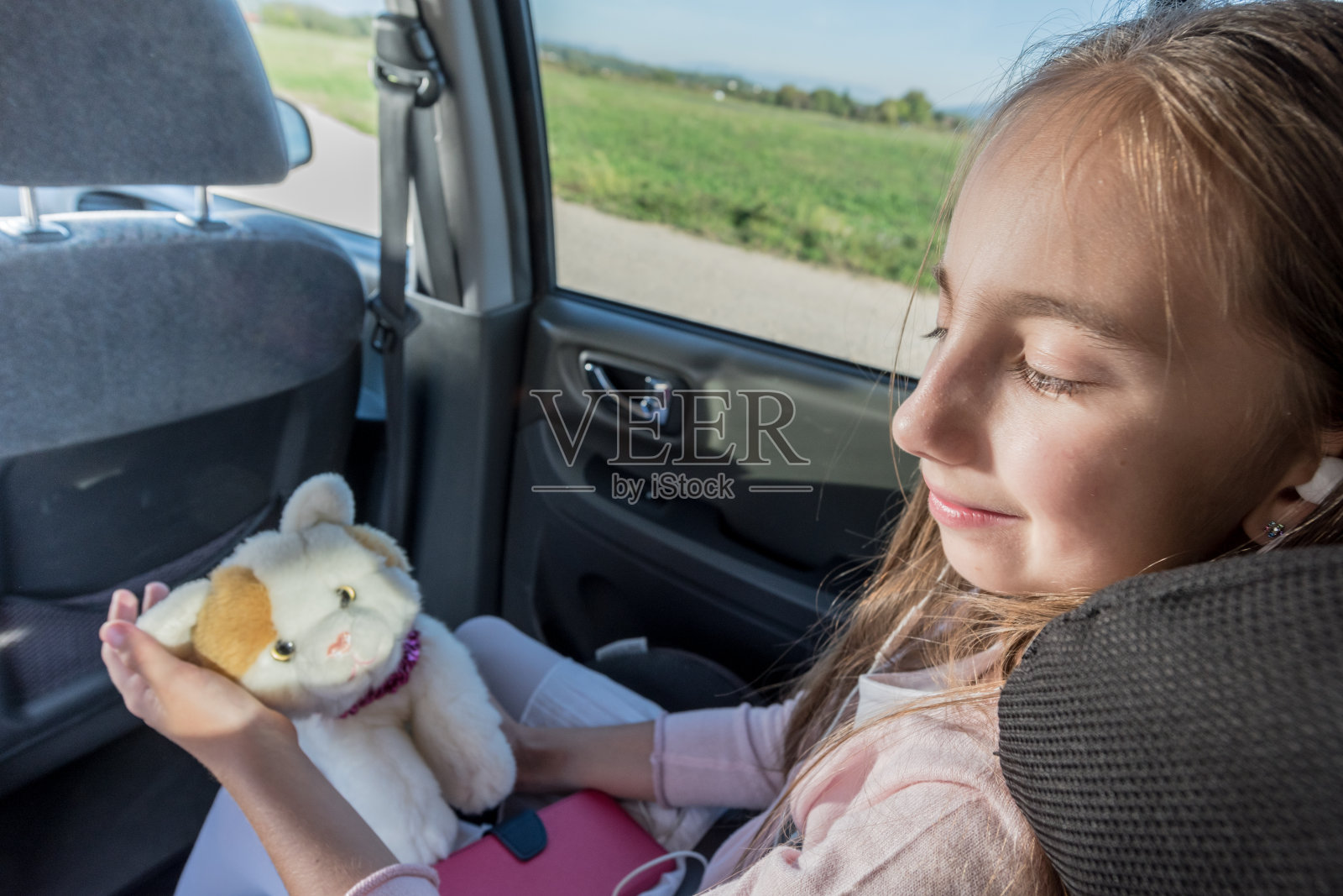 快乐的女孩玩她的毛绒猫和听音乐坐在汽车座位上在公路旅行照片摄影图片