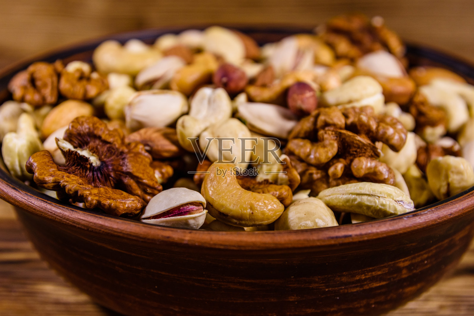 各种坚果(杏仁、腰果、榛子、开心果、核桃)放在陶瓷盘子里，放在木桌上。素食餐。健康饮食的概念照片摄影图片
