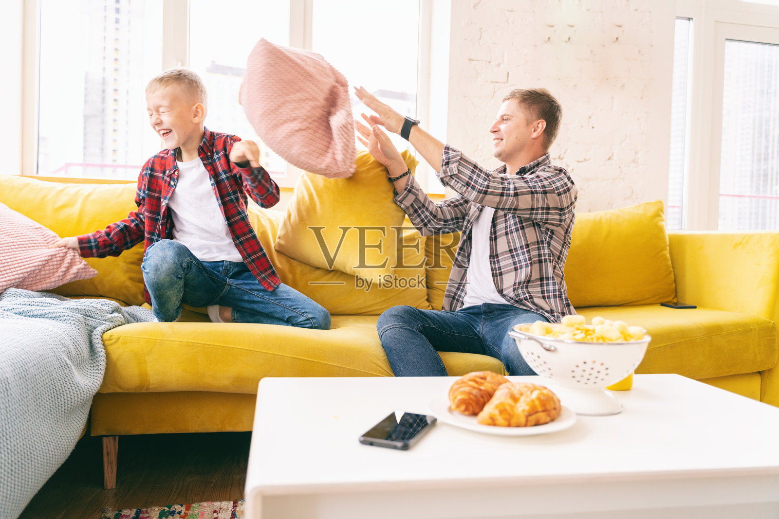 年轻的父亲和一个儿子，一个8岁的男孩在格子衬衫，战斗枕头，在一起快乐的时间照片摄影图片