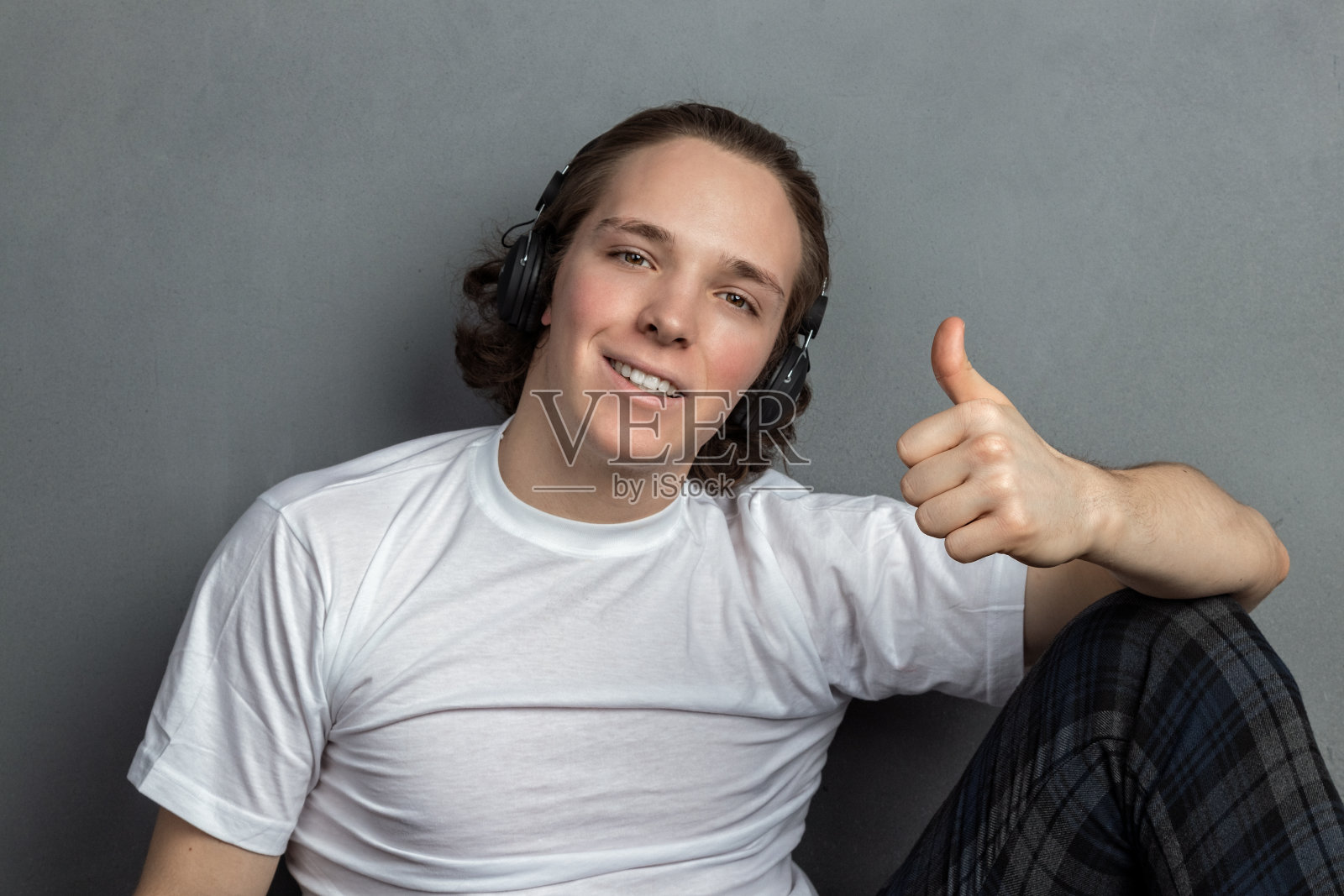 英俊的年轻人坐在客厅的地板上，头上戴着耳机听着音乐照片摄影图片