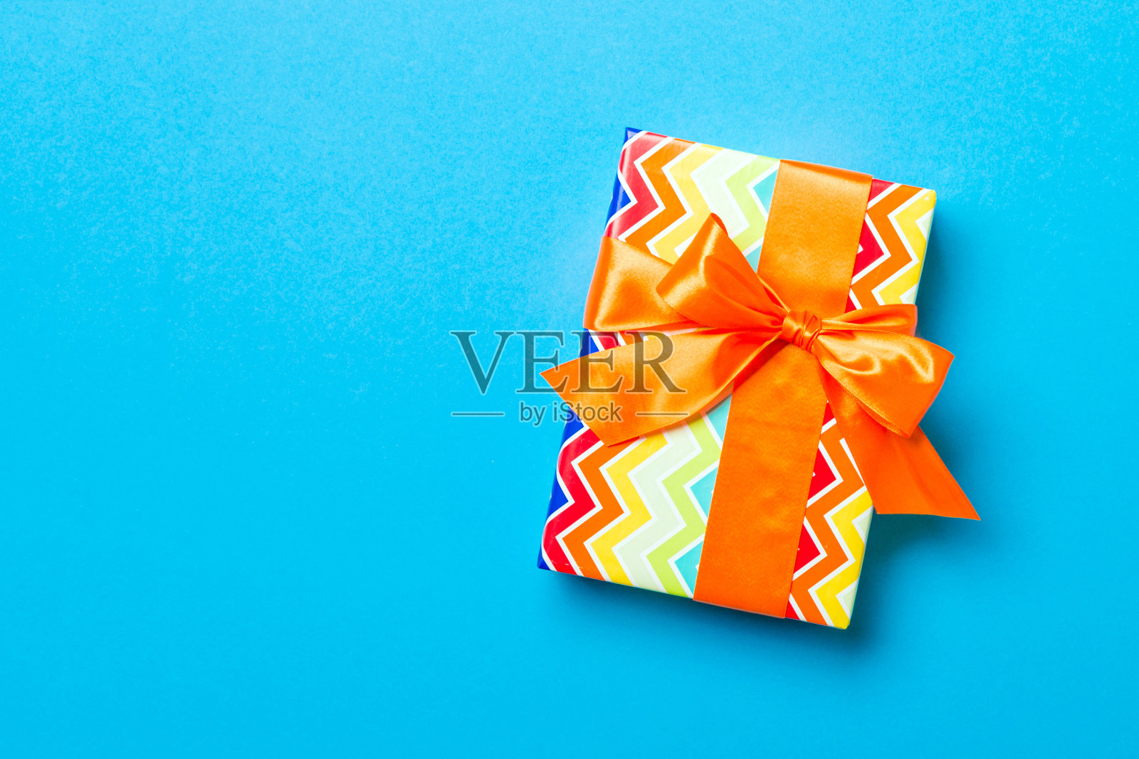 用橙色丝带和蓝色背景纸包好的圣诞节或其他节日手工礼物。礼品盒，彩桌上礼品装饰，顶视图有拷贝空间照片摄影图片