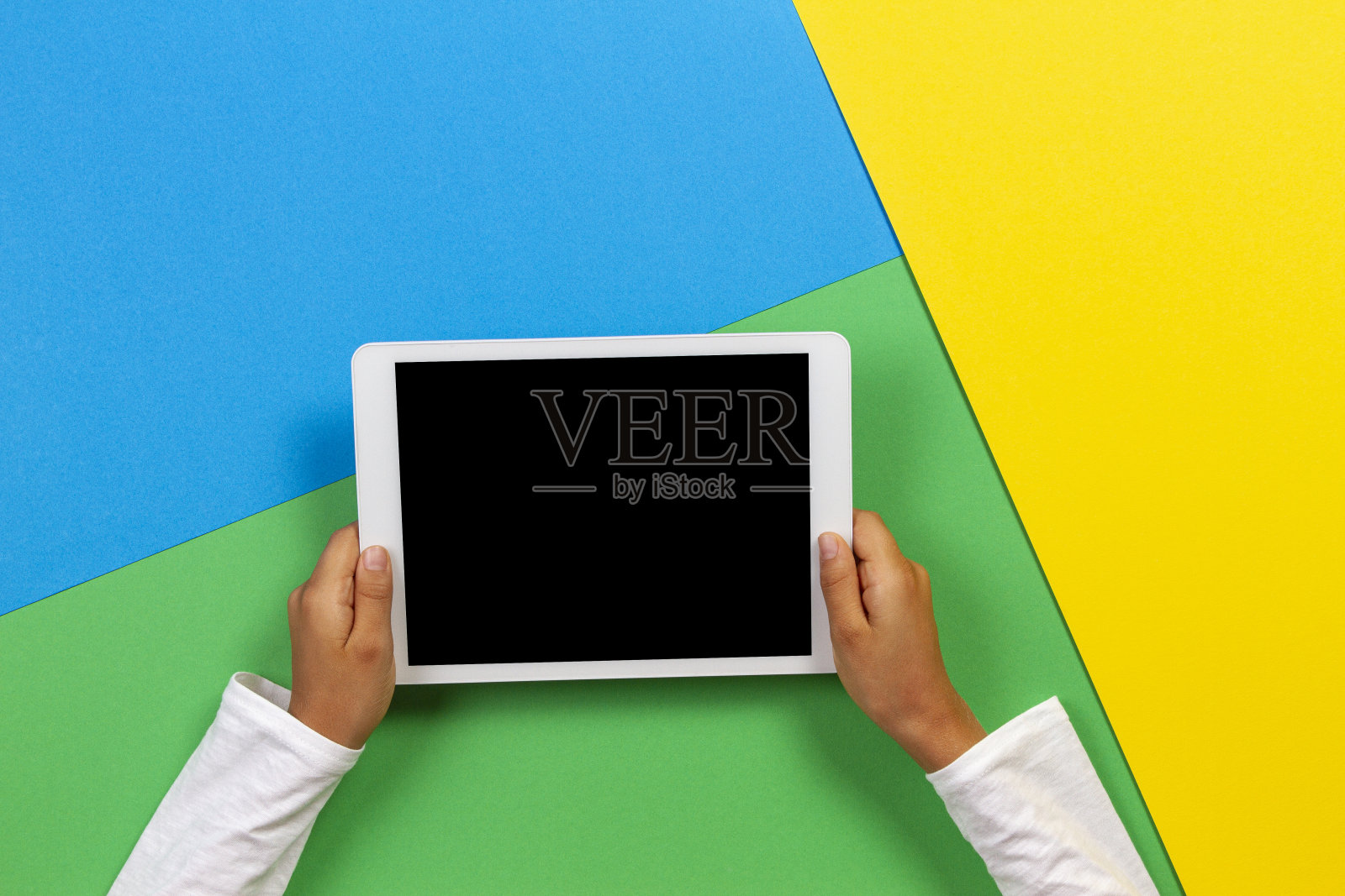 孩子的手与平板电脑在黄色，蓝色和绿色的背景照片摄影图片