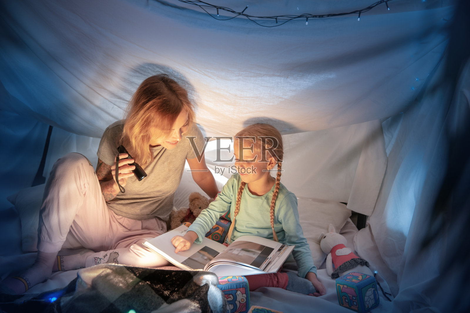 母亲和女儿坐在帐篷里，拿着手电筒读故事照片摄影图片
