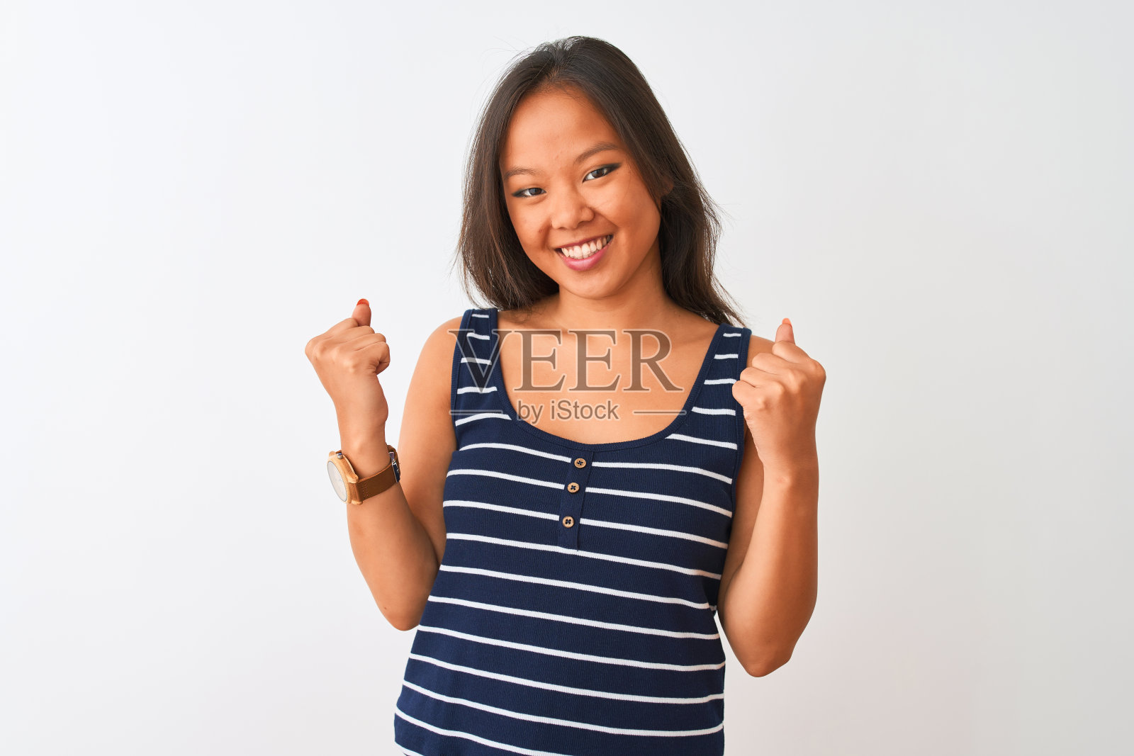 年轻的中国女人穿着条纹t恤站在孤立的白色背景非常高兴和兴奋做胜利者的姿态，举起手臂，微笑和尖叫的成功。庆祝活动的概念。照片摄影图片