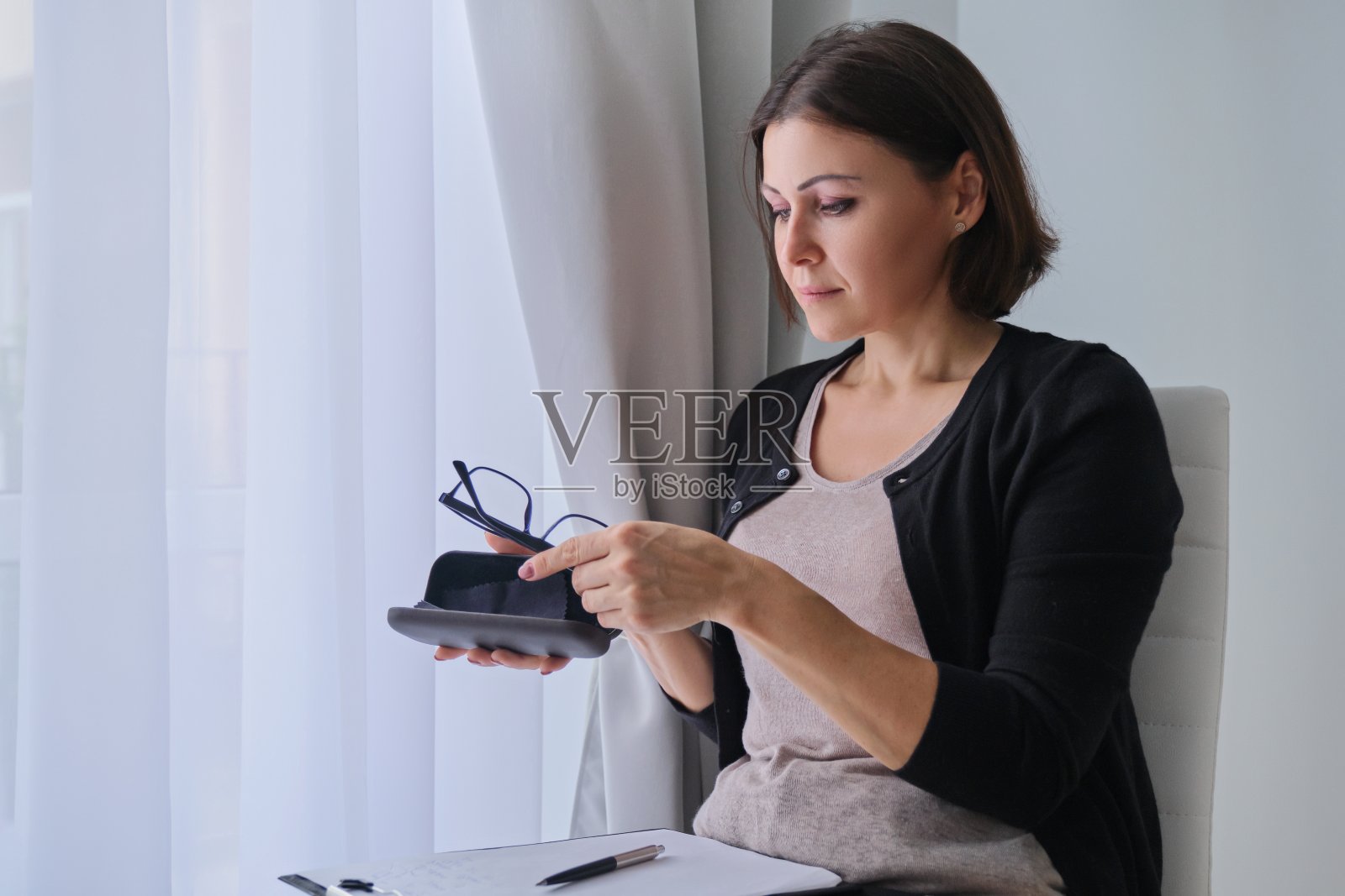 严肃成熟的女商人，戴着眼镜坐在窗边照片摄影图片