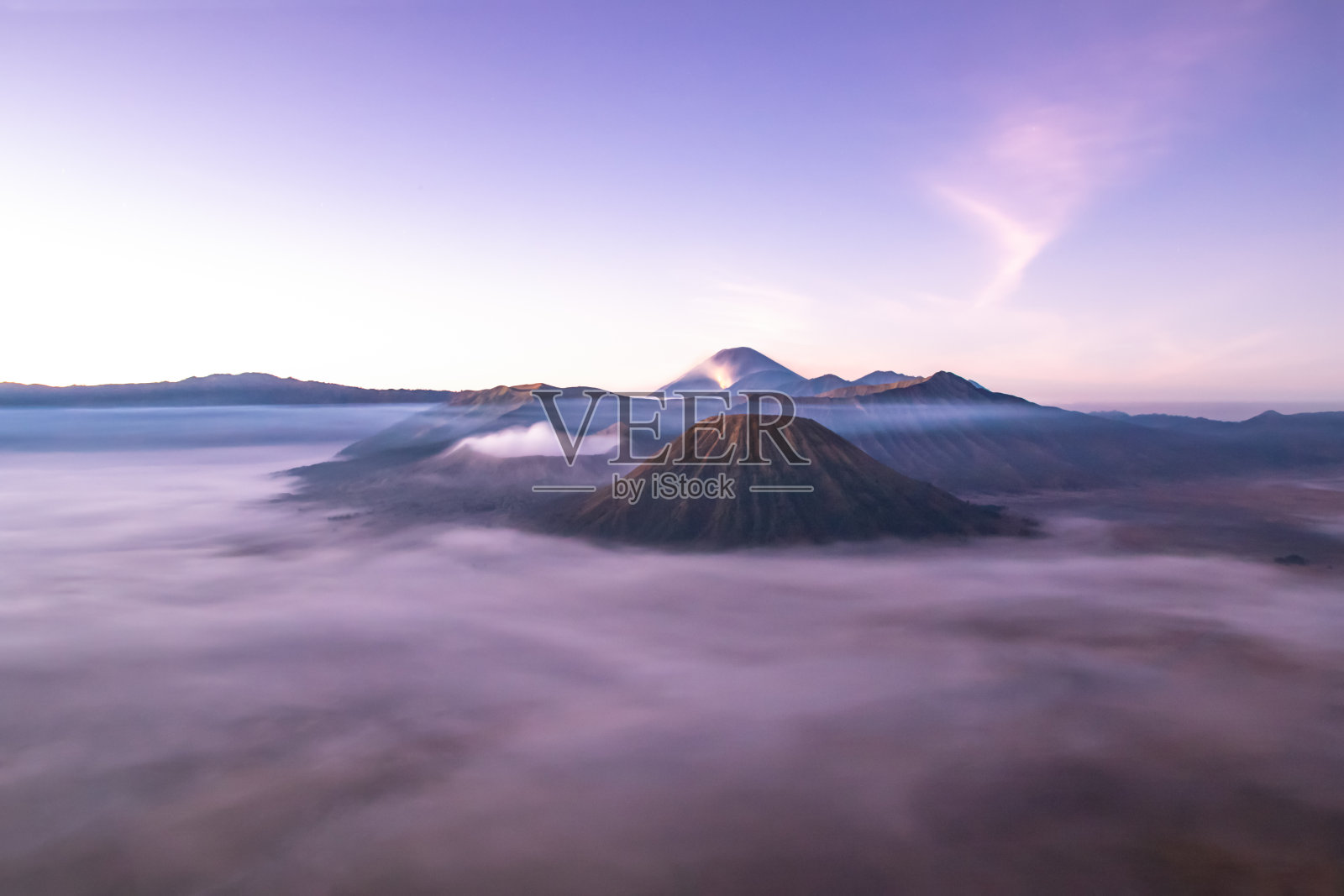 日出时的布罗莫山。云在山谷;气体从火山口升起。火焰在峰值的背景。照片摄影图片