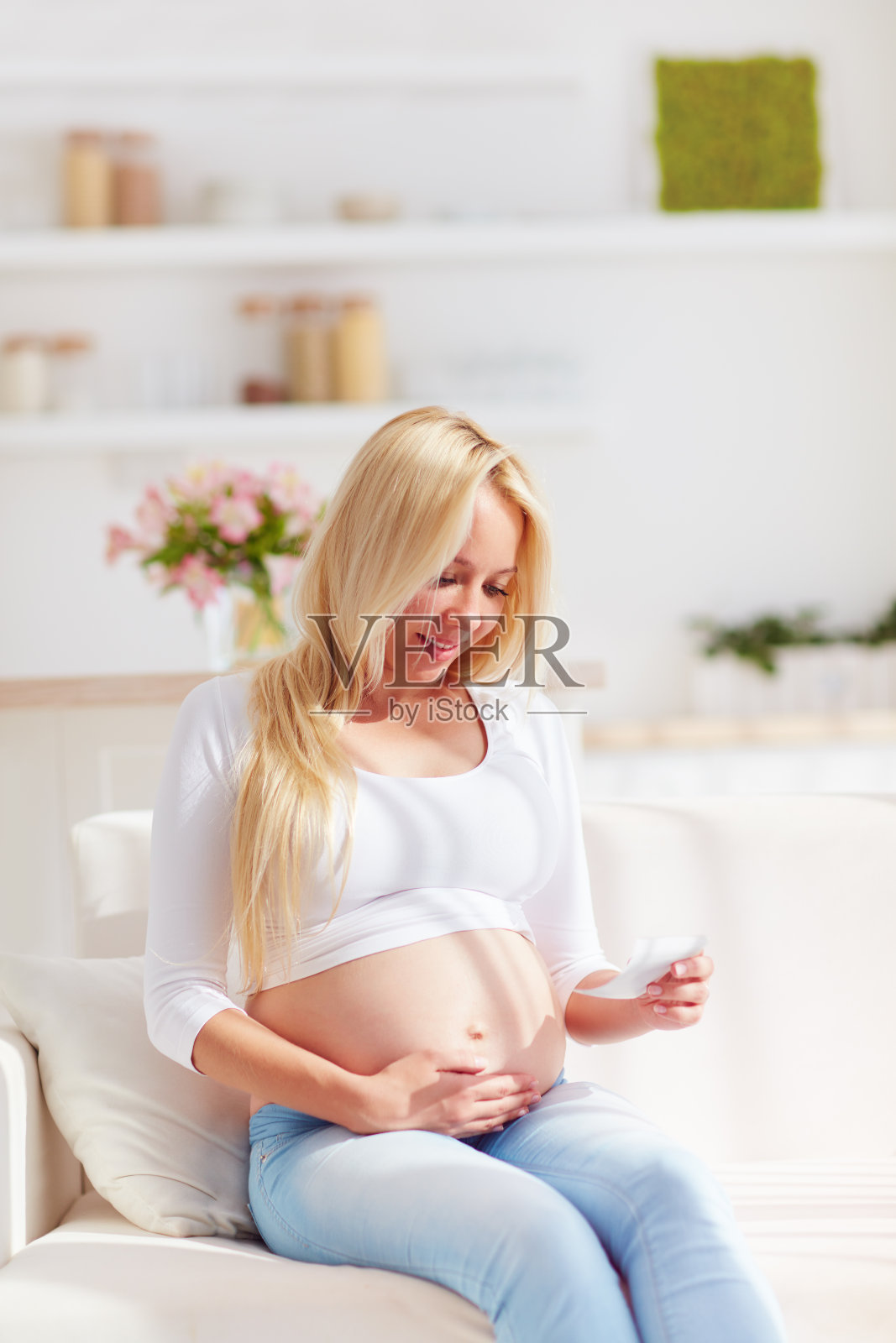 快乐的孕妇抱着超声波照片，坐在家里的沙发上照片摄影图片