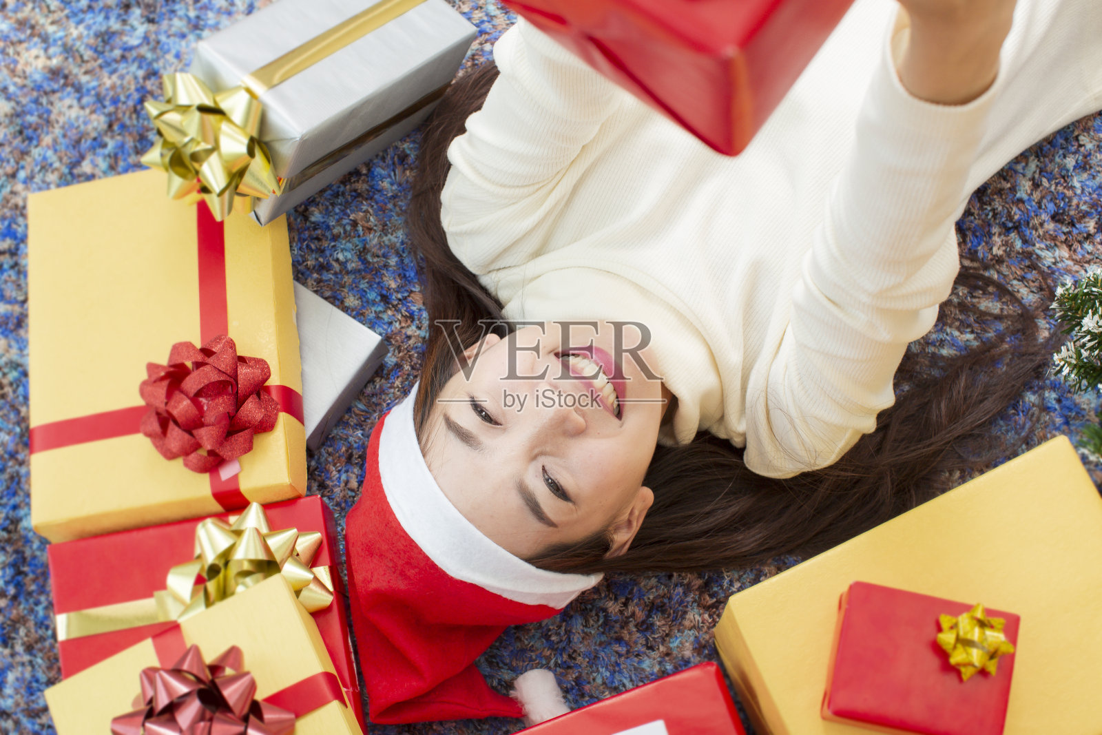 圣诞快乐和节日快乐的概念。快乐女性与礼盒。年轻妇女戴着圣诞帽，手里拿着用金纸和红丝带包裹的礼物。照片摄影图片