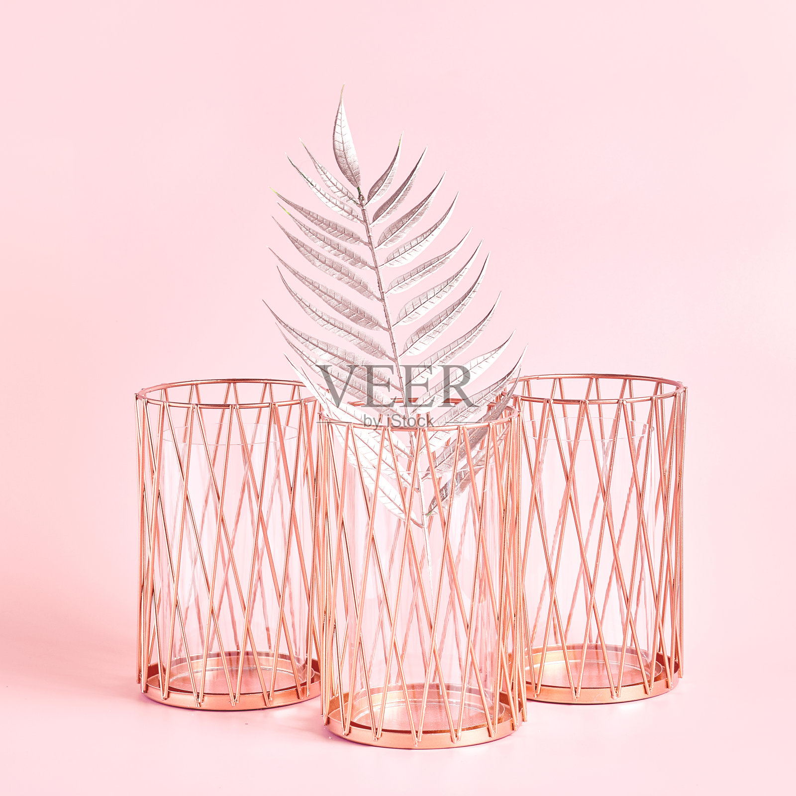 由三个金属烛台和一个热带树叶颜色的玫瑰金在浅粉色的背景。家居装饰，方框照片摄影图片