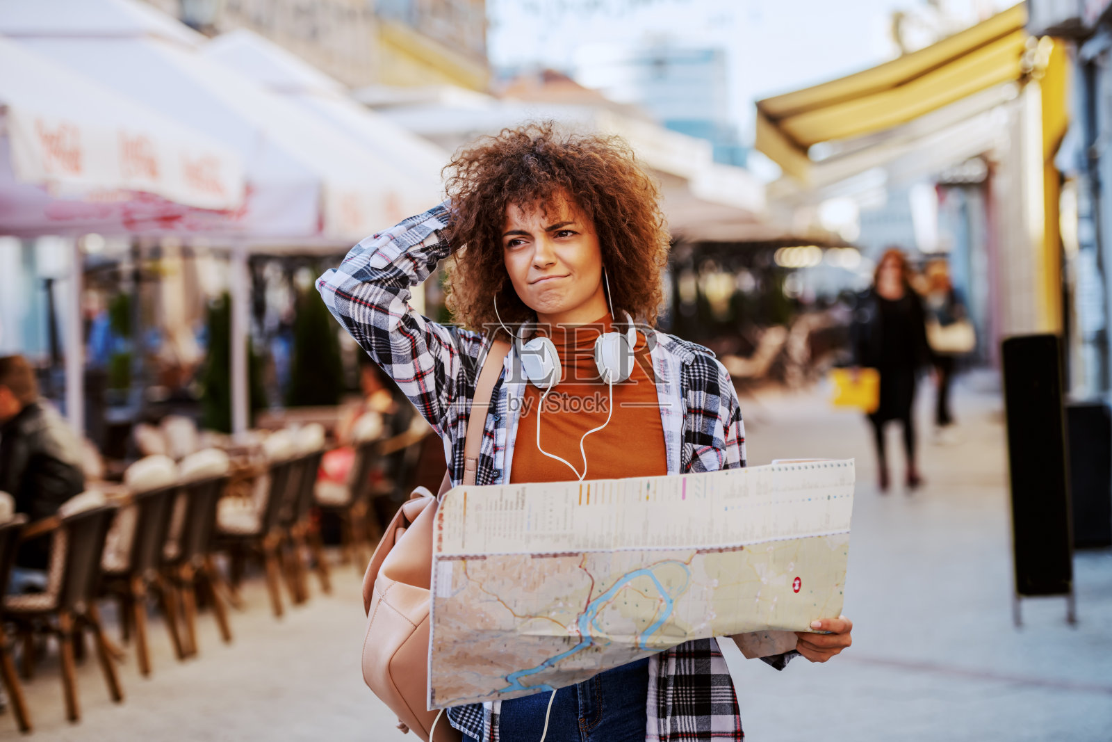 迷失的年轻混血女游客与卷发和格子衬衫拿着城市地图和看哪里去，而站在主要街道。照片摄影图片
