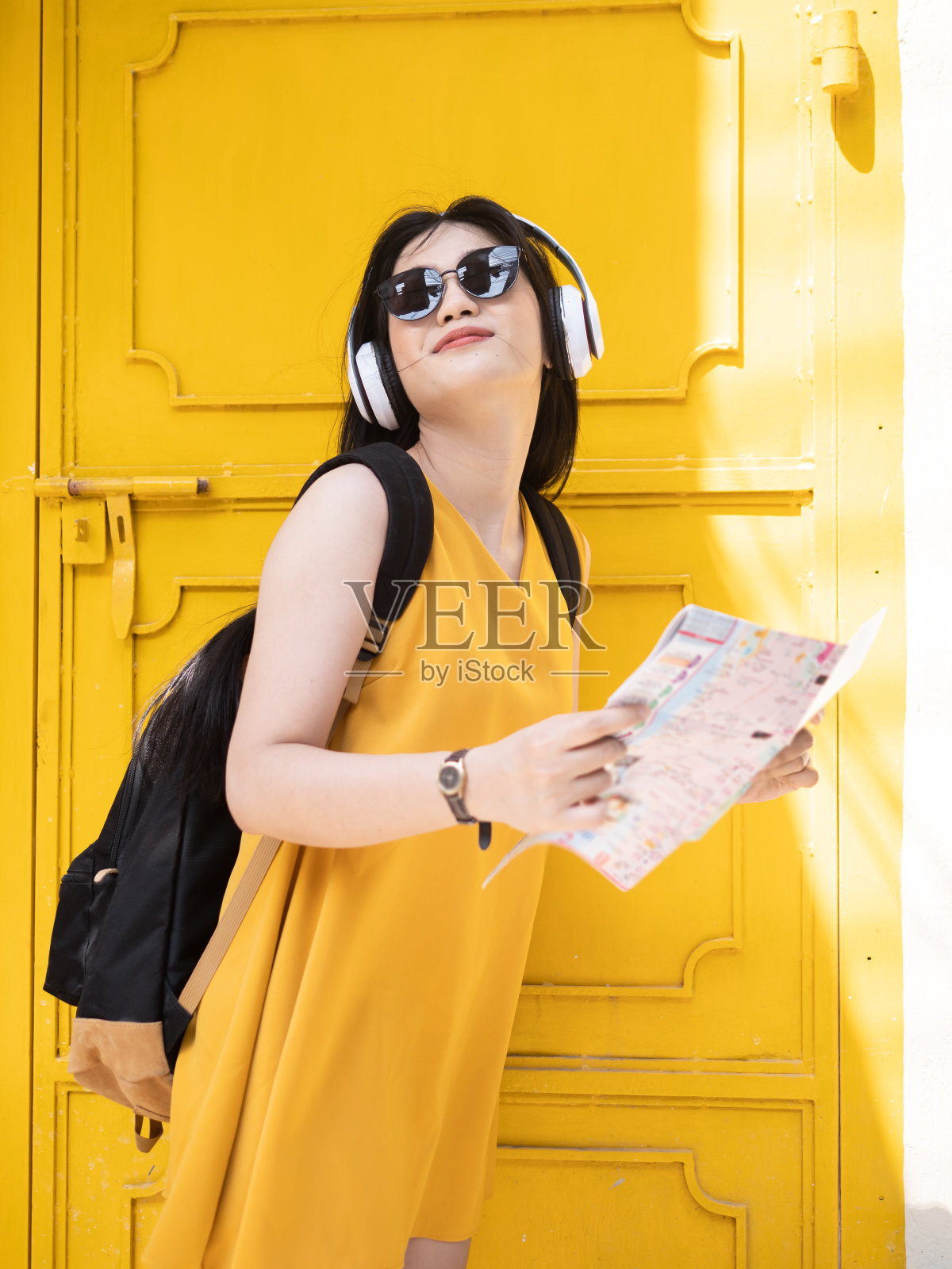 亚洲女性背包使用耳机和拿着地图在城市，旅游的概念。照片摄影图片