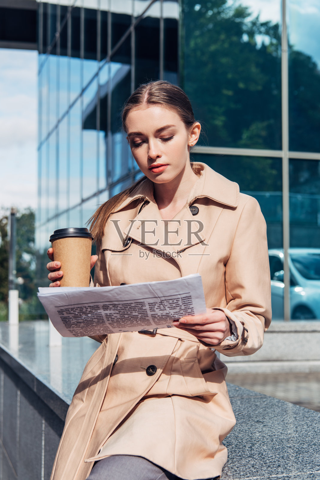 穿着风衣的美女拿着纸杯看报纸照片摄影图片