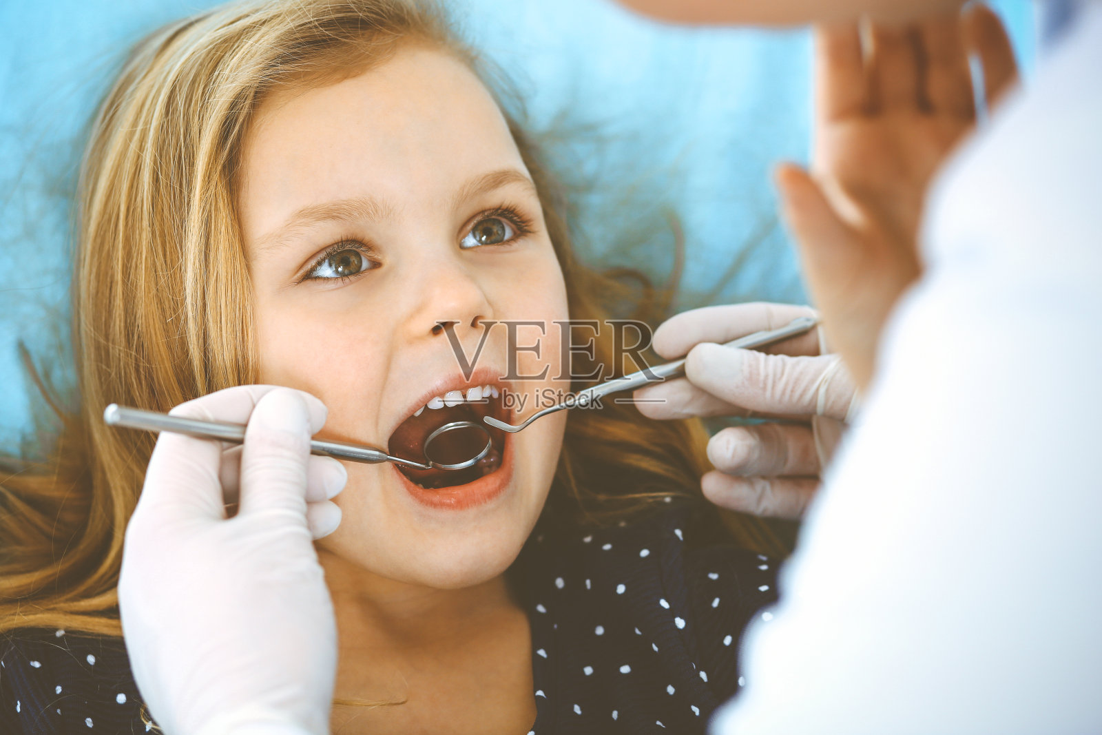 小女孩张大嘴巴坐在牙科椅上接受医生的口腔检查。拜访牙医的办公室。医学概念。健美的照片照片摄影图片