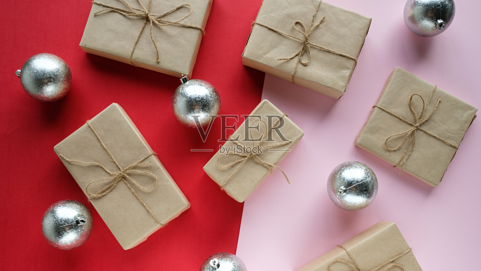 圣诞礼物放在红粉色的背景上，旁边是银色的圣诞球。照片摄影图片