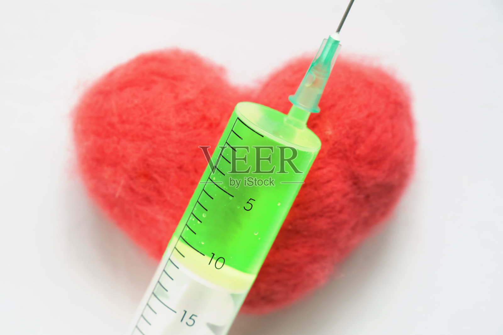 注射器，绿色的药躺在红色的心脏上照片摄影图片