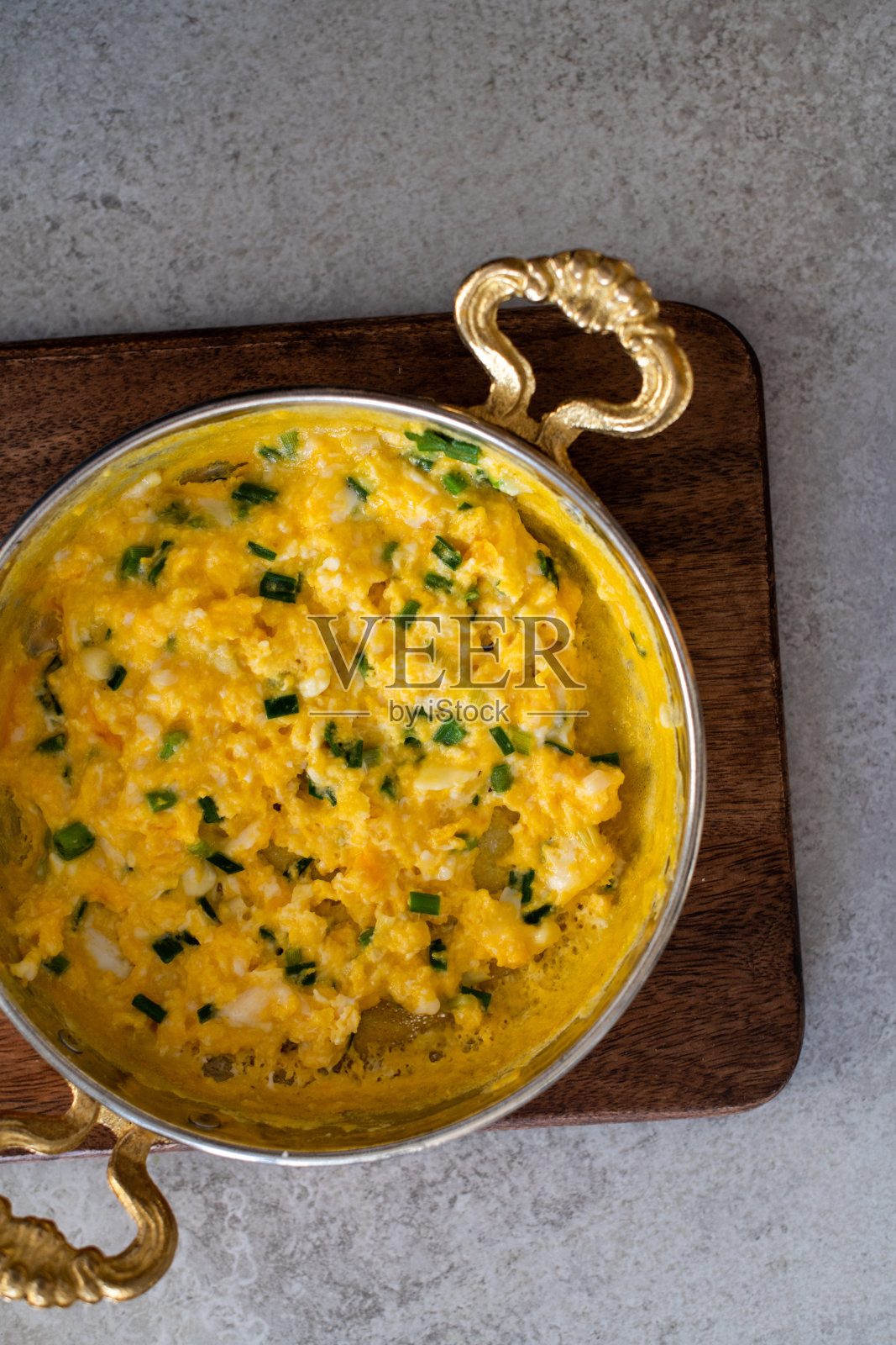 芝士炒蛋和葱。盛在铜锅里。照片摄影图片