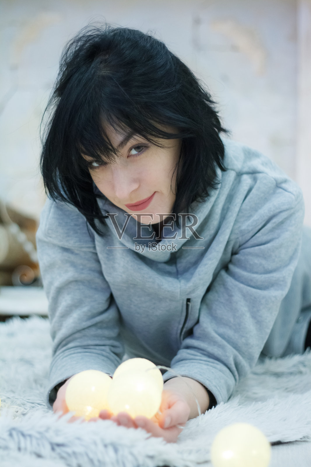 幸福迷人的黑发女孩躺在家里，带着花环的灯光，选择性聚焦照片摄影图片