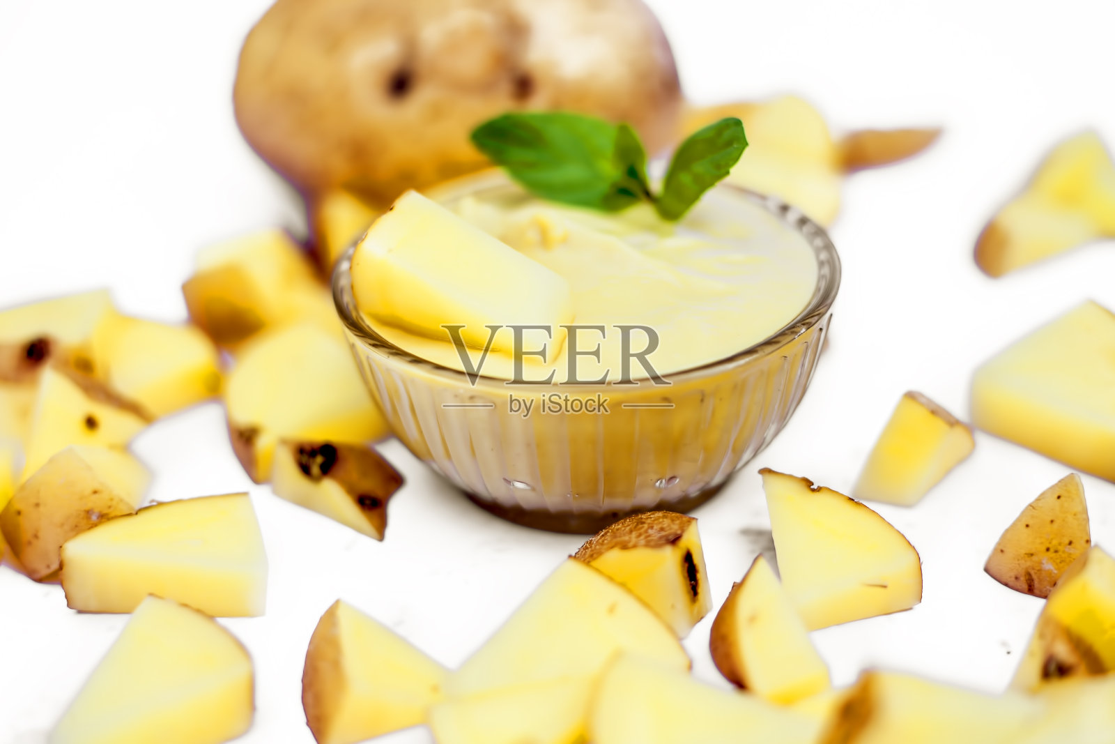 近距离拍摄的生切土豆连同煮糊或泥在一个玻璃碗与一些薄荷叶孤立在一个白色的表面。水平。照片摄影图片