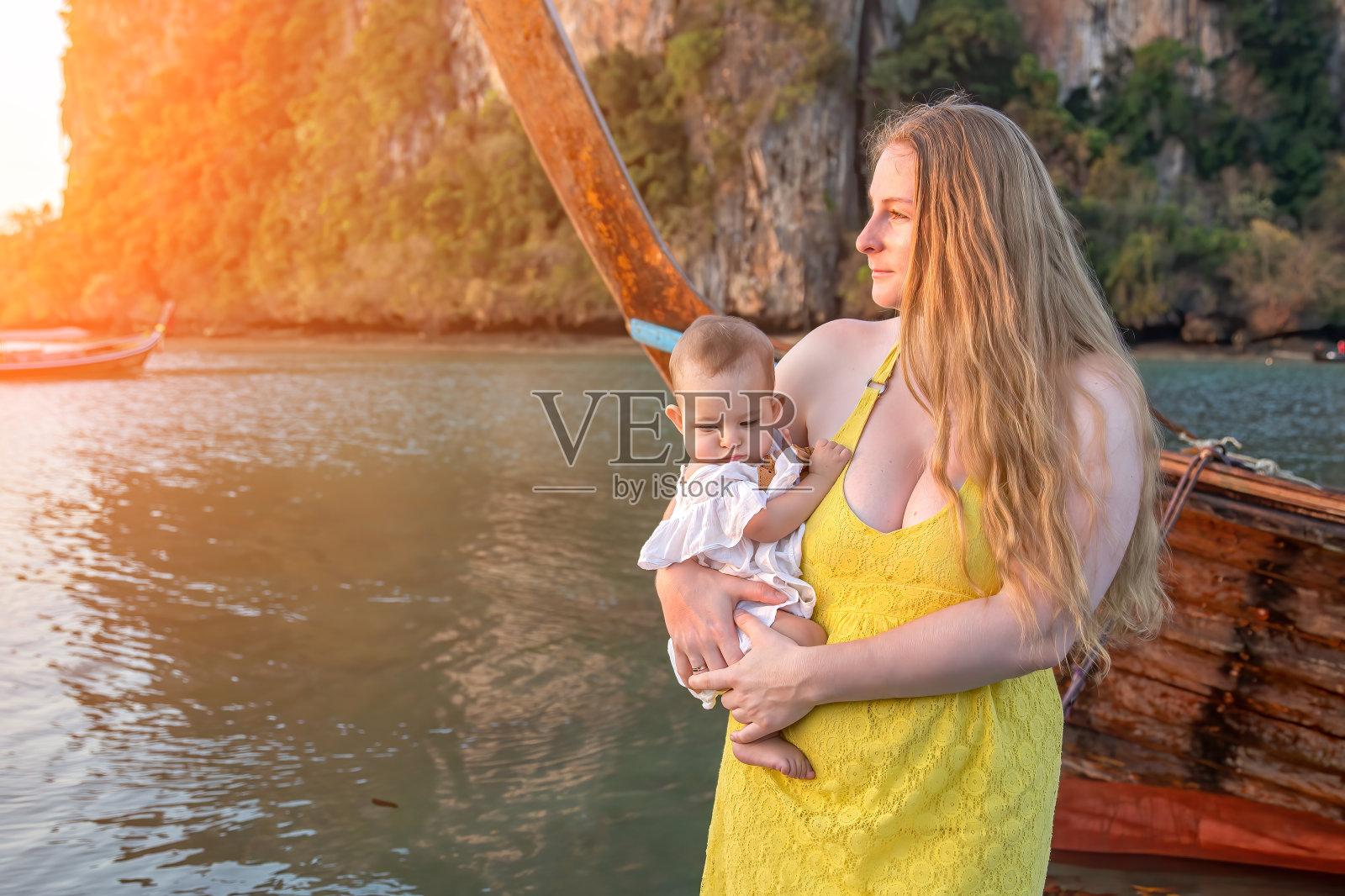 清晨，妈妈带着孩子站在水的背景上，在热带海滩上迎接日出。照片摄影图片