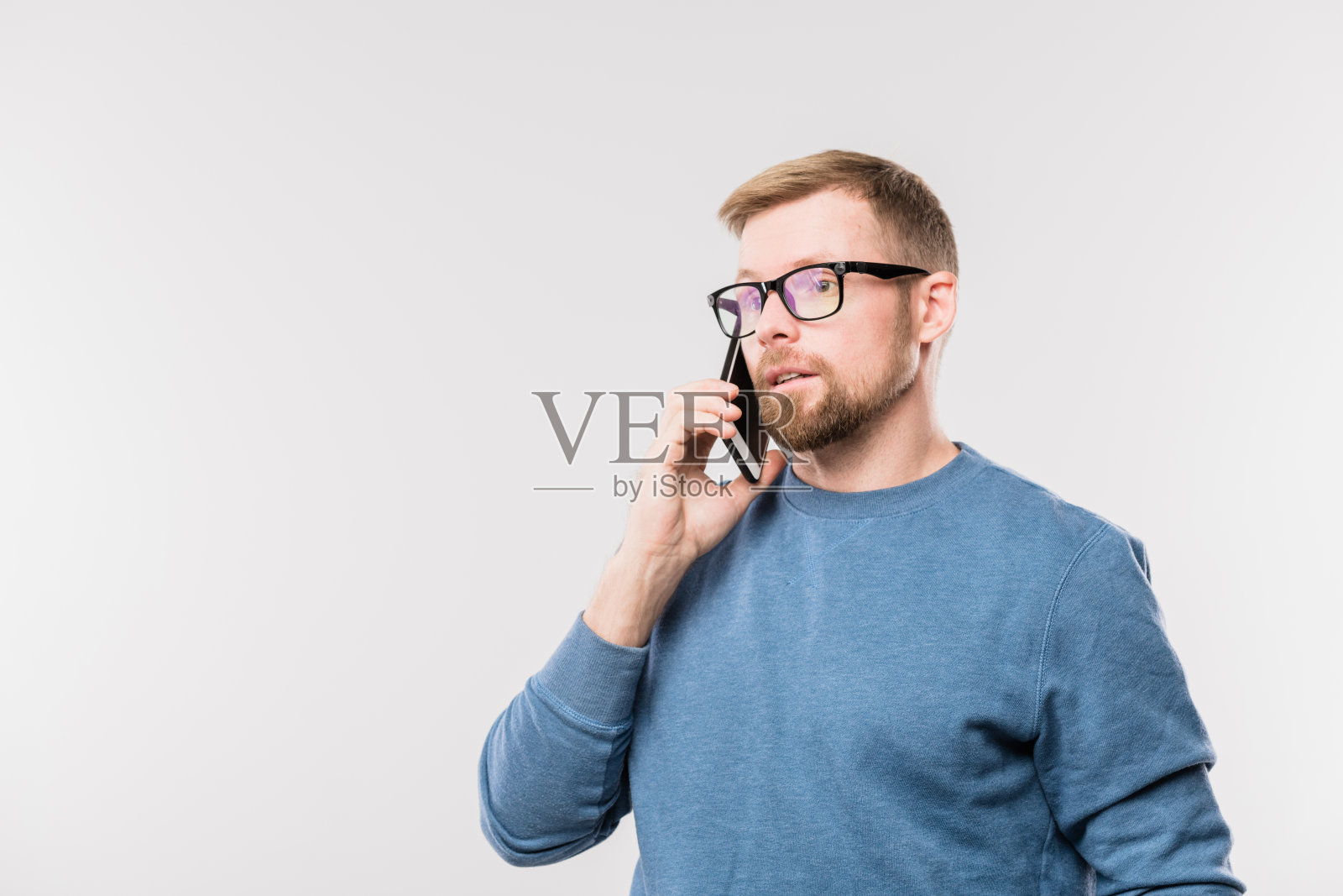 一名留着胡子的年轻特工在和一名客户说话时，把智能手机挂在耳朵上照片摄影图片