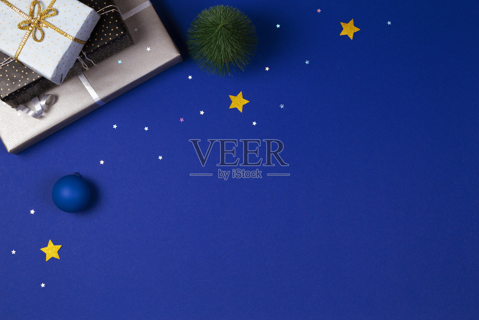 圣诞礼物包装的礼物纸，小圣诞树，蓝色背景上缀着闪闪发光的星星的小装饰品。圣诞节、新年、假日概念照片摄影图片