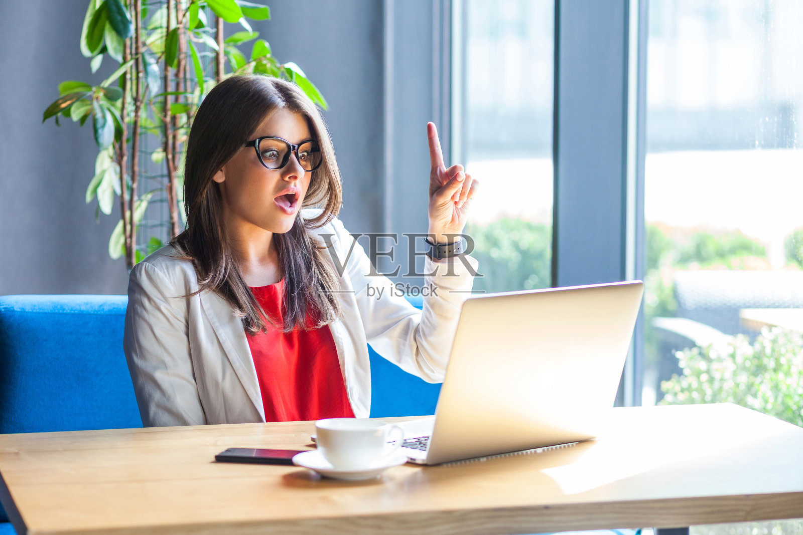 我有个主意。肖像惊讶美丽时尚的黑发年轻女子在眼镜坐，看着她的笔记本电脑屏幕的想法手势和惊讶。照片摄影图片