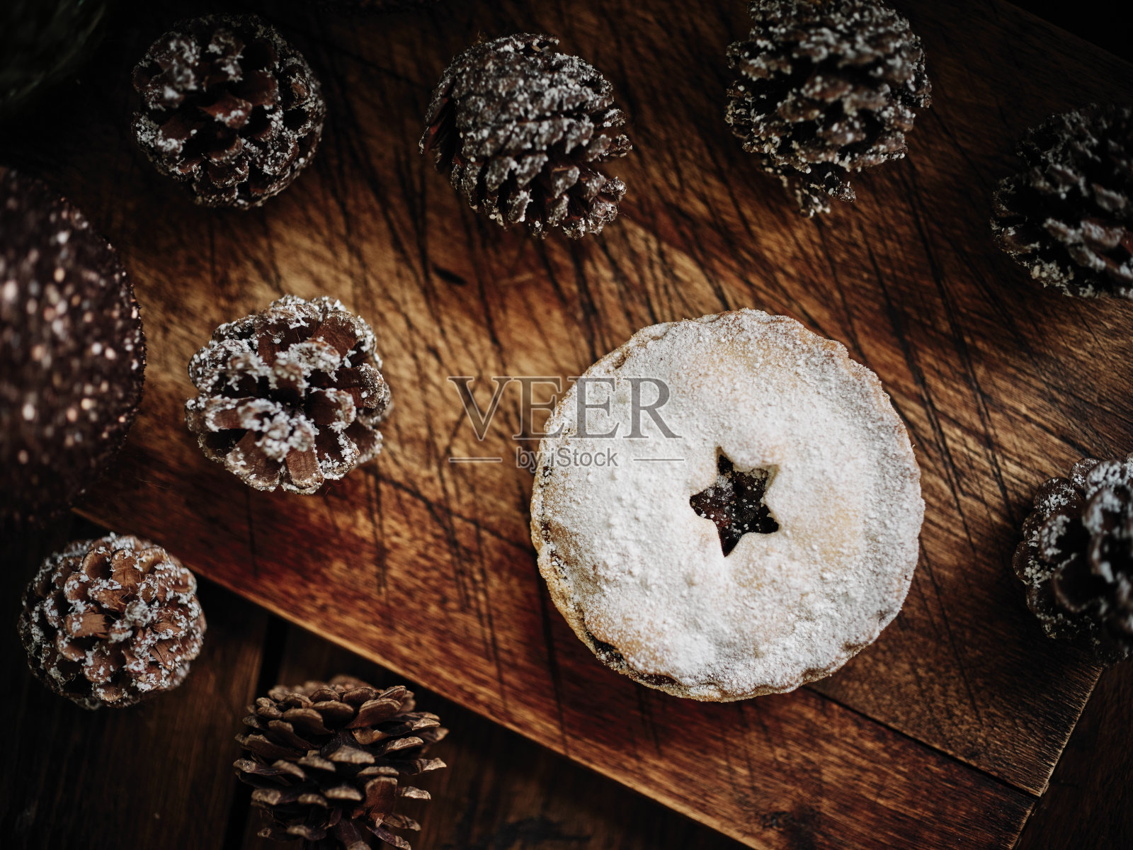 肉馅馅饼对着深色的木材表面，周围是覆盖着雪的节日松果。照片摄影图片