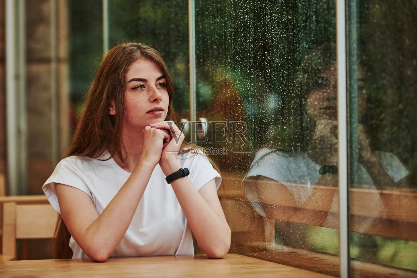 下雨天坐在咖啡馆里的年轻女孩的肖像。一个人只有照片摄影图片