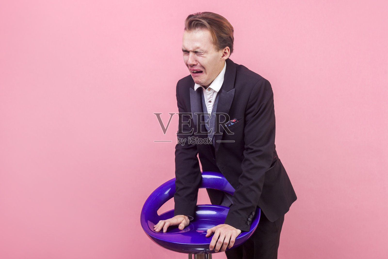 一个极度绝望的男人带着痛苦的表情哭喊着。孤立在粉红色背景上照片摄影图片