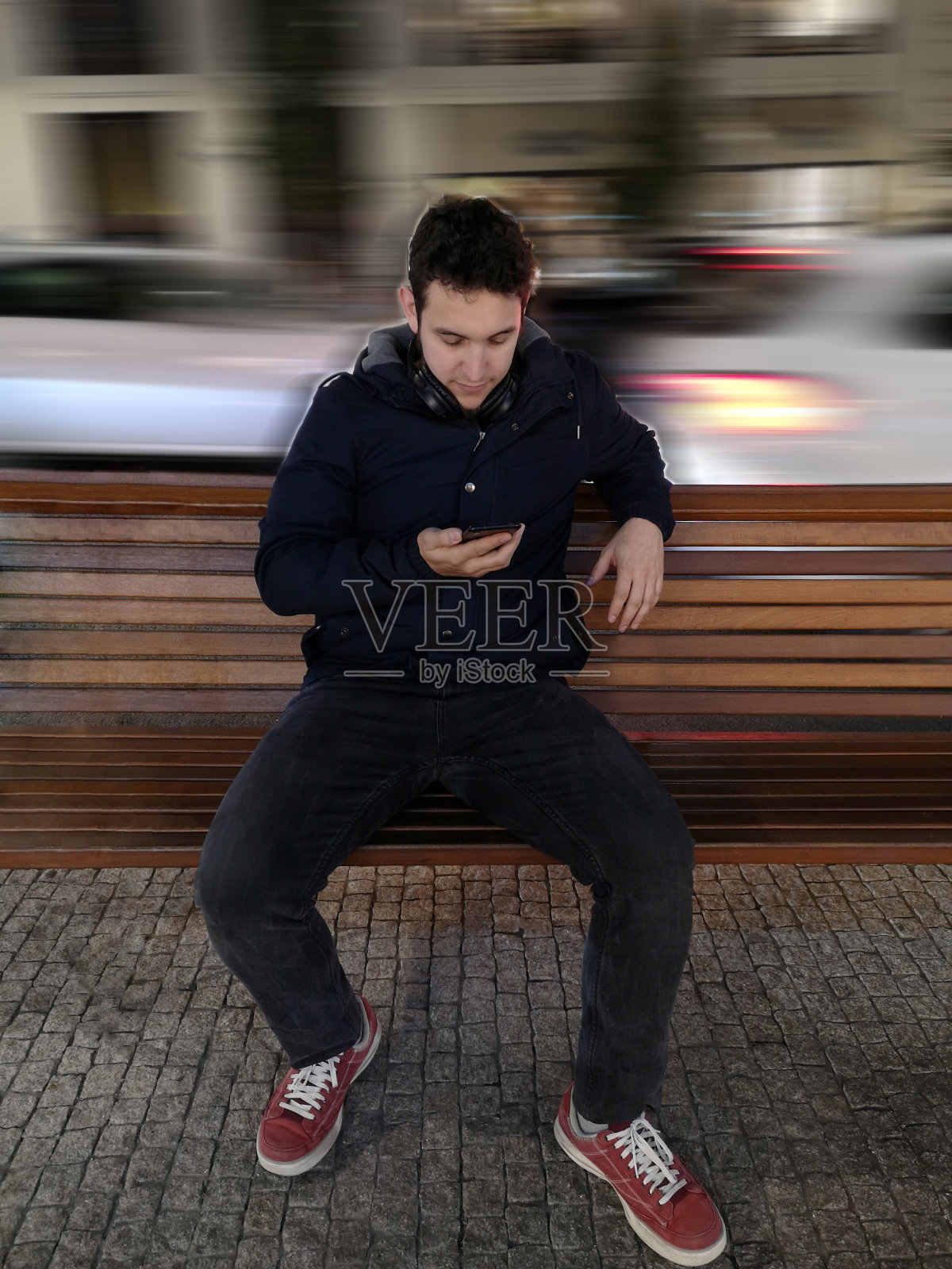 一个拉丁年轻人坐在长凳上看他的手机照片摄影图片