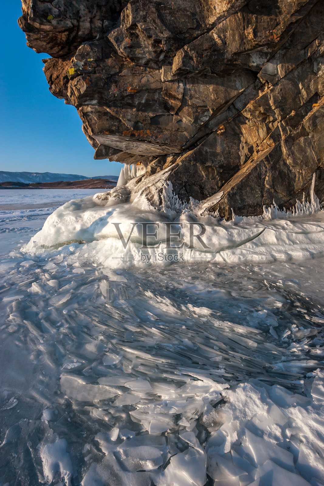 贝加尔湖上的一块大岩石旁边有许多薄薄的碎冰板。照片摄影图片