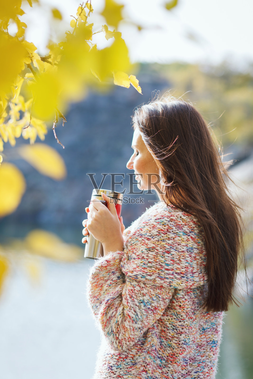 年轻女子与杯上湖的背景在秋天的一天。照片摄影图片