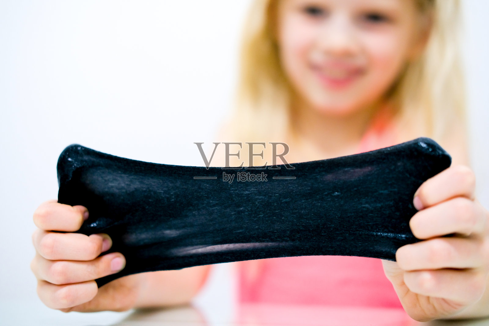 金发女孩把黑色黏液伸展到身体两侧。孩子们用手玩黏液玩具。使粘液。Copyspace。有选择性的重点照片摄影图片