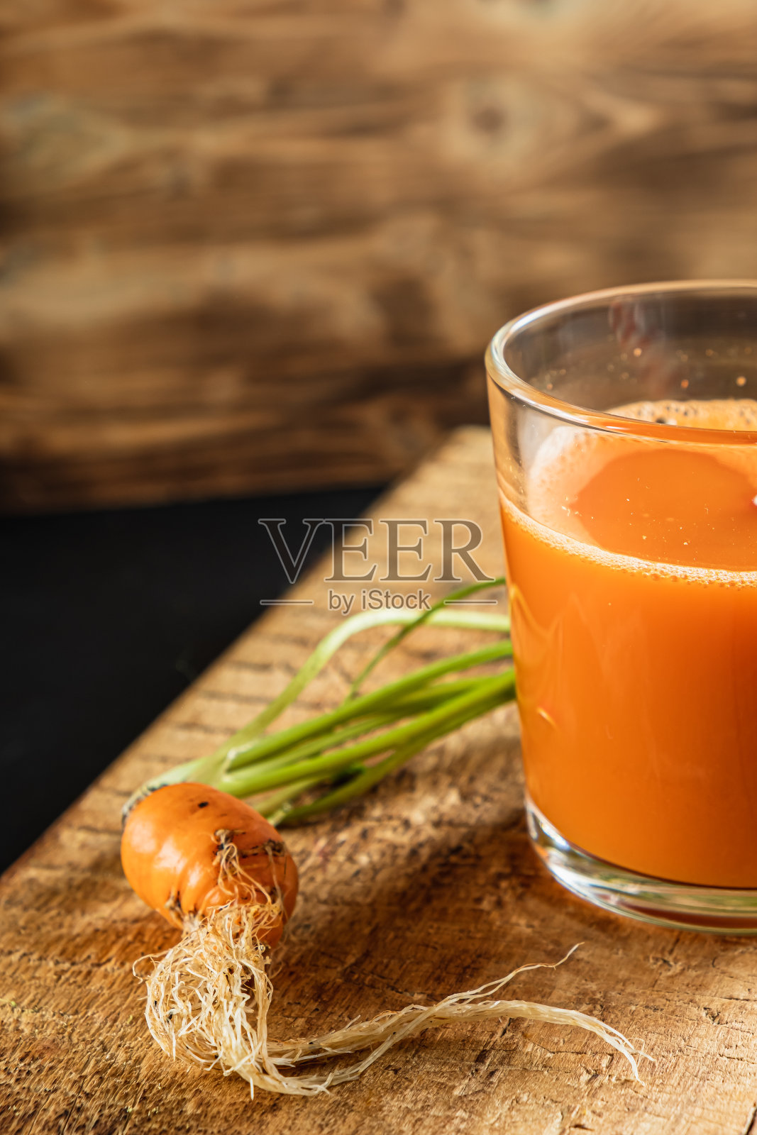 一个丑陋的小胡萝卜。一杯鲜榨胡萝卜汁。一个长着绿叶的丑陋胡萝卜。塑料是免费的。垂直orentecion照片摄影图片