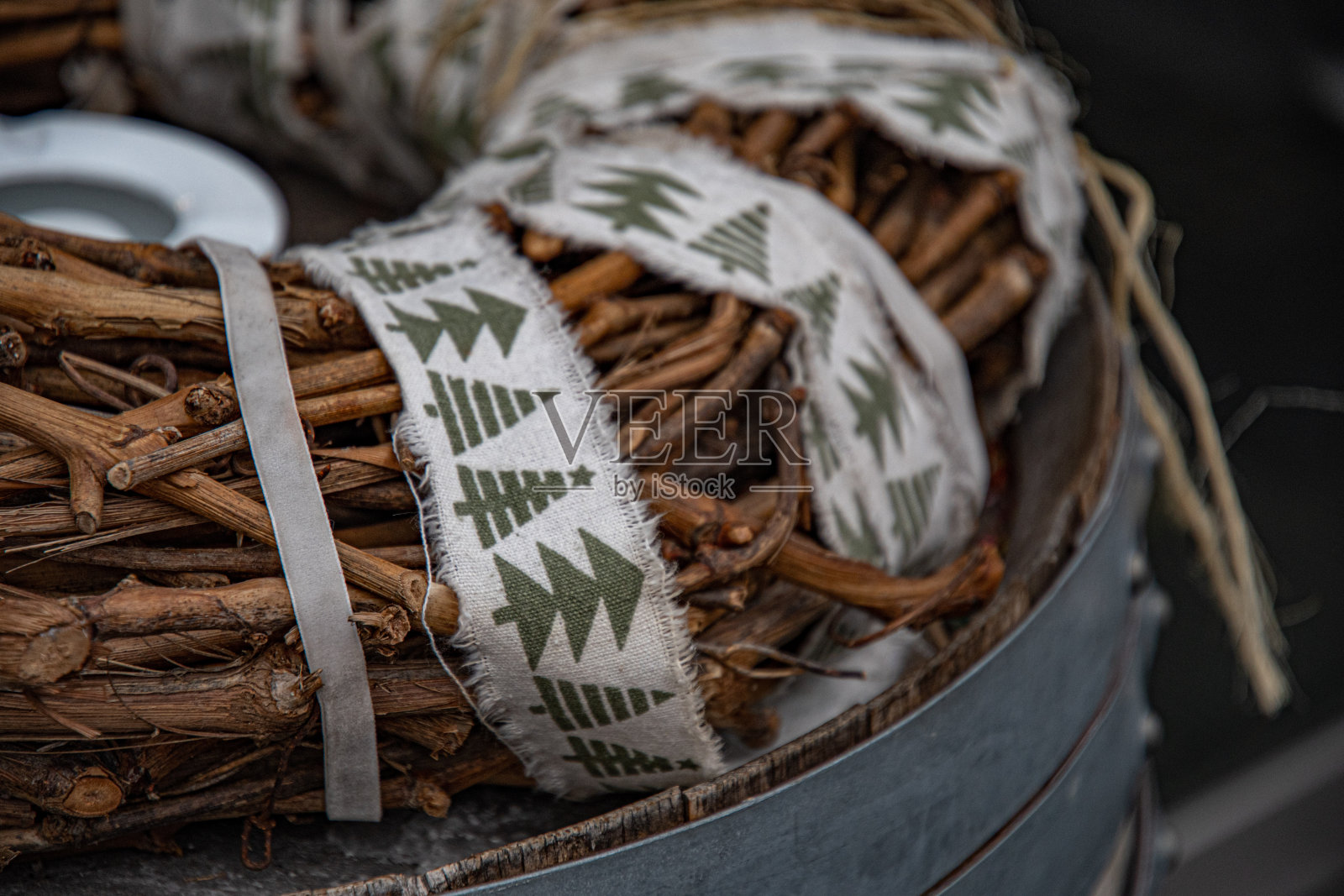 用棕色的葡萄藤枝编织而成的圣诞花环，用麻线和肮脏的白丝带包裹，上面有圣诞树的原始绿色图案。顶部的旧桶与铆接金属箍。照片摄影图片