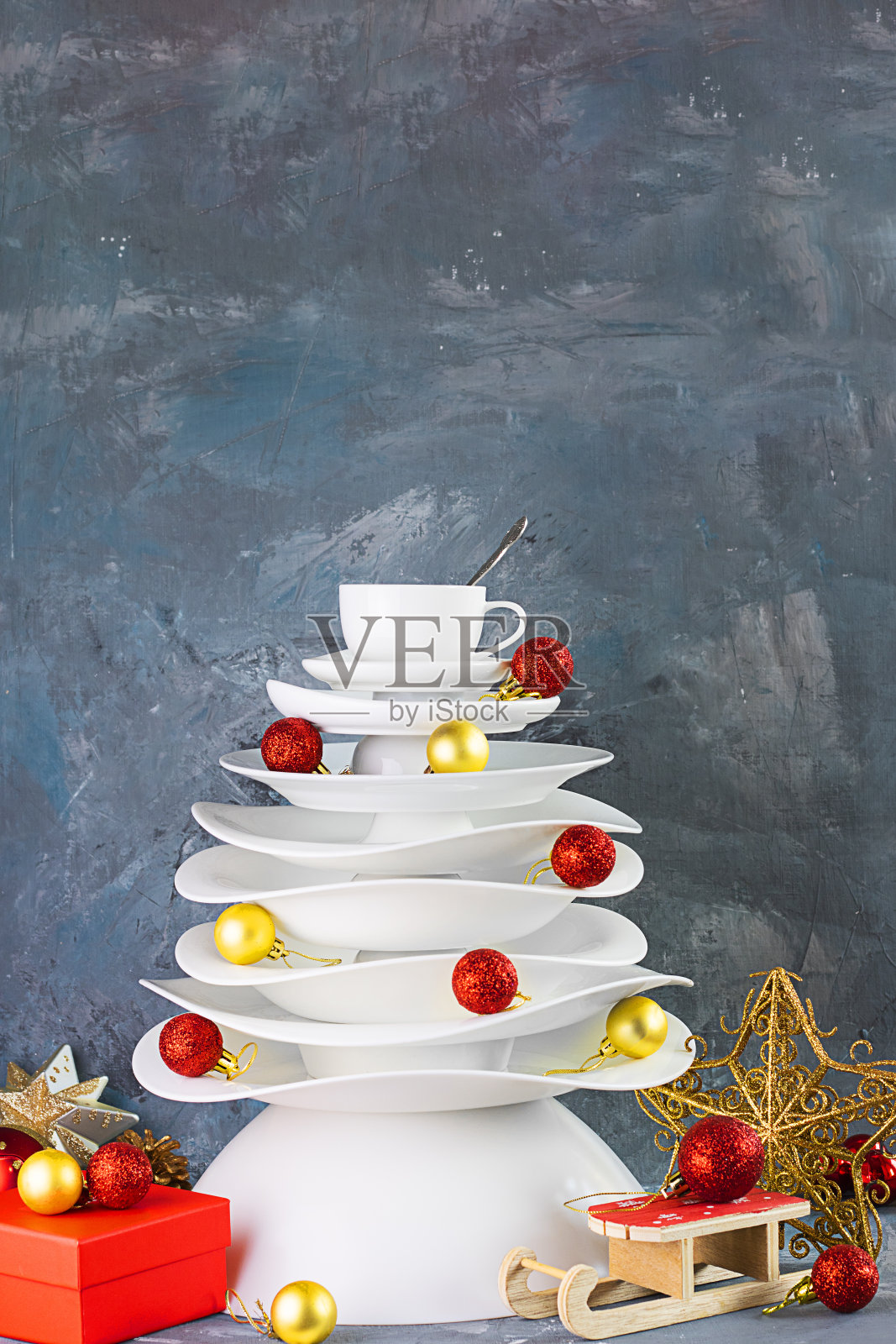 陶瓷白色盘子圣诞树与黄色和红色的圣诞球，礼物盒在黑暗的背景下。垂直的。创意概念，明信片食物，餐厅，菜单，派对，餐具照片摄影图片