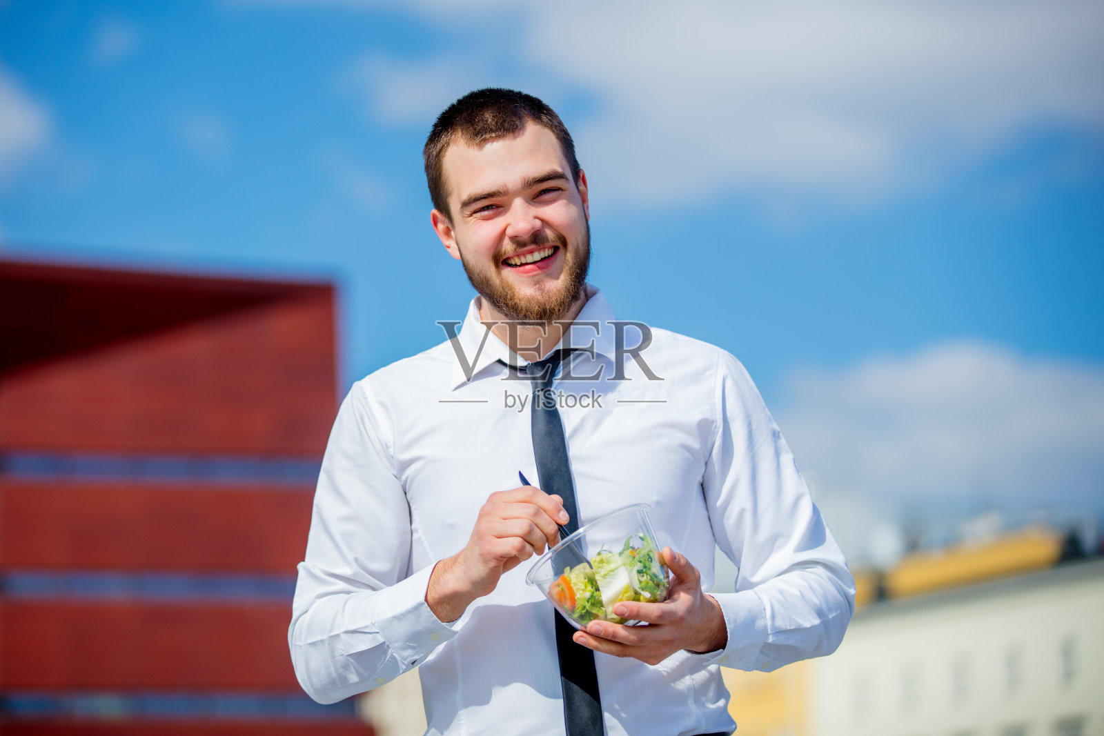 年轻的商人穿着衬衫，打着领带，带着沙拉午餐盒照片摄影图片
