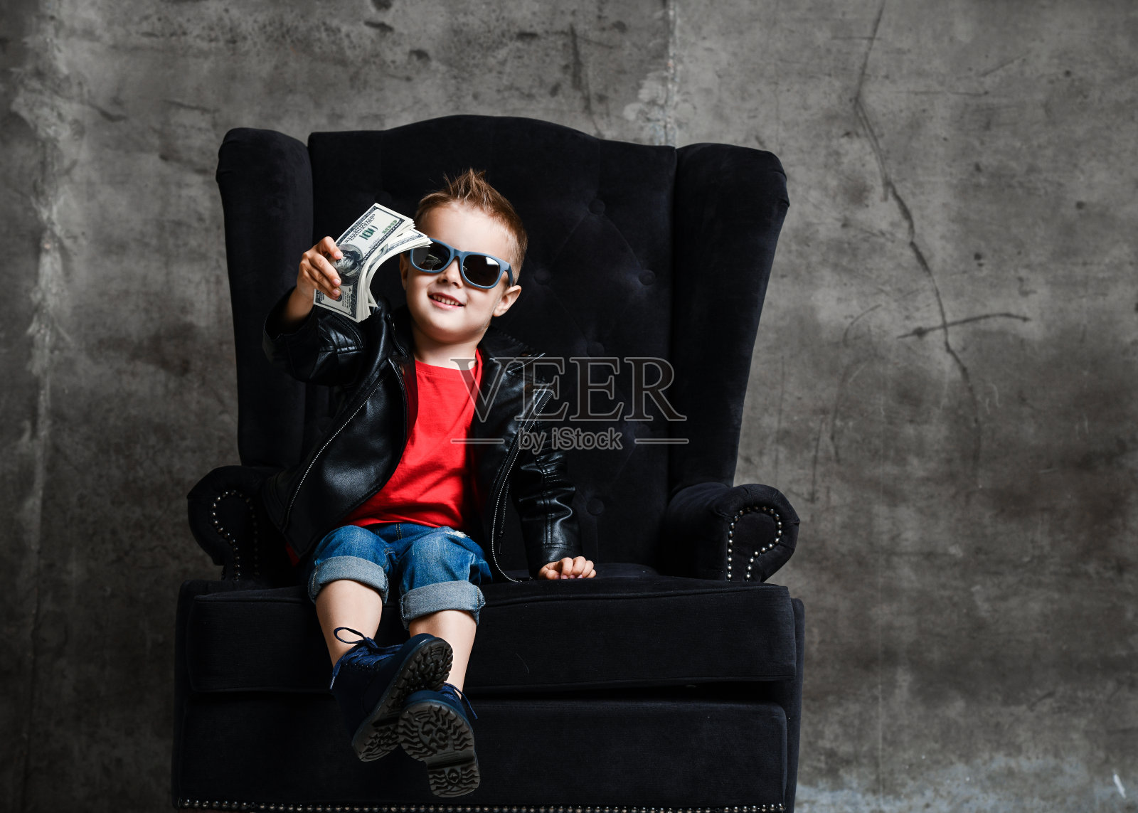 穿着皮夹克和红色t恤的百万富翁坐在豪华的扶手椅上递给我们一捆现金照片摄影图片