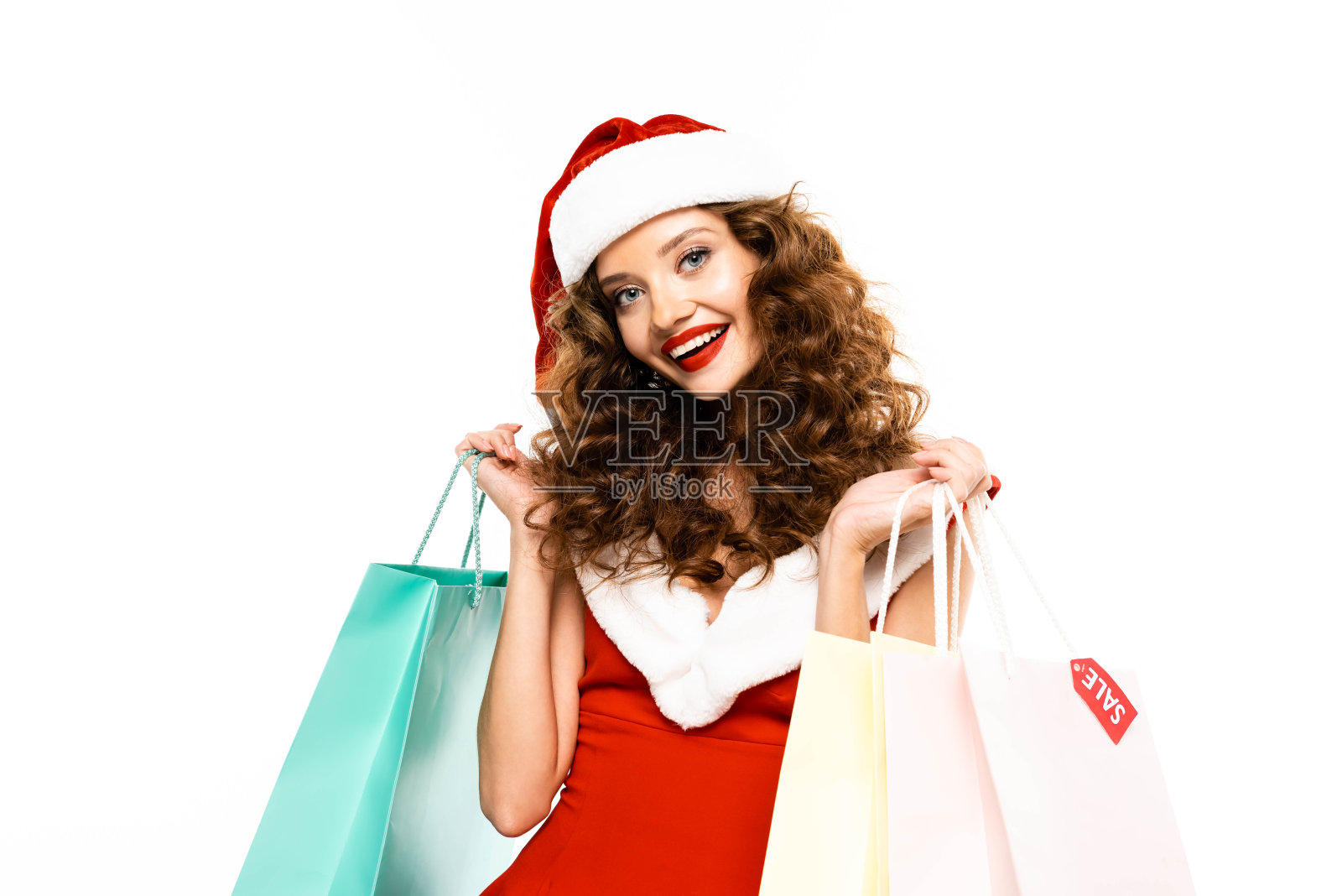 微笑的女孩在圣诞老人服装与购物袋摆姿势，孤立在白色照片摄影图片
