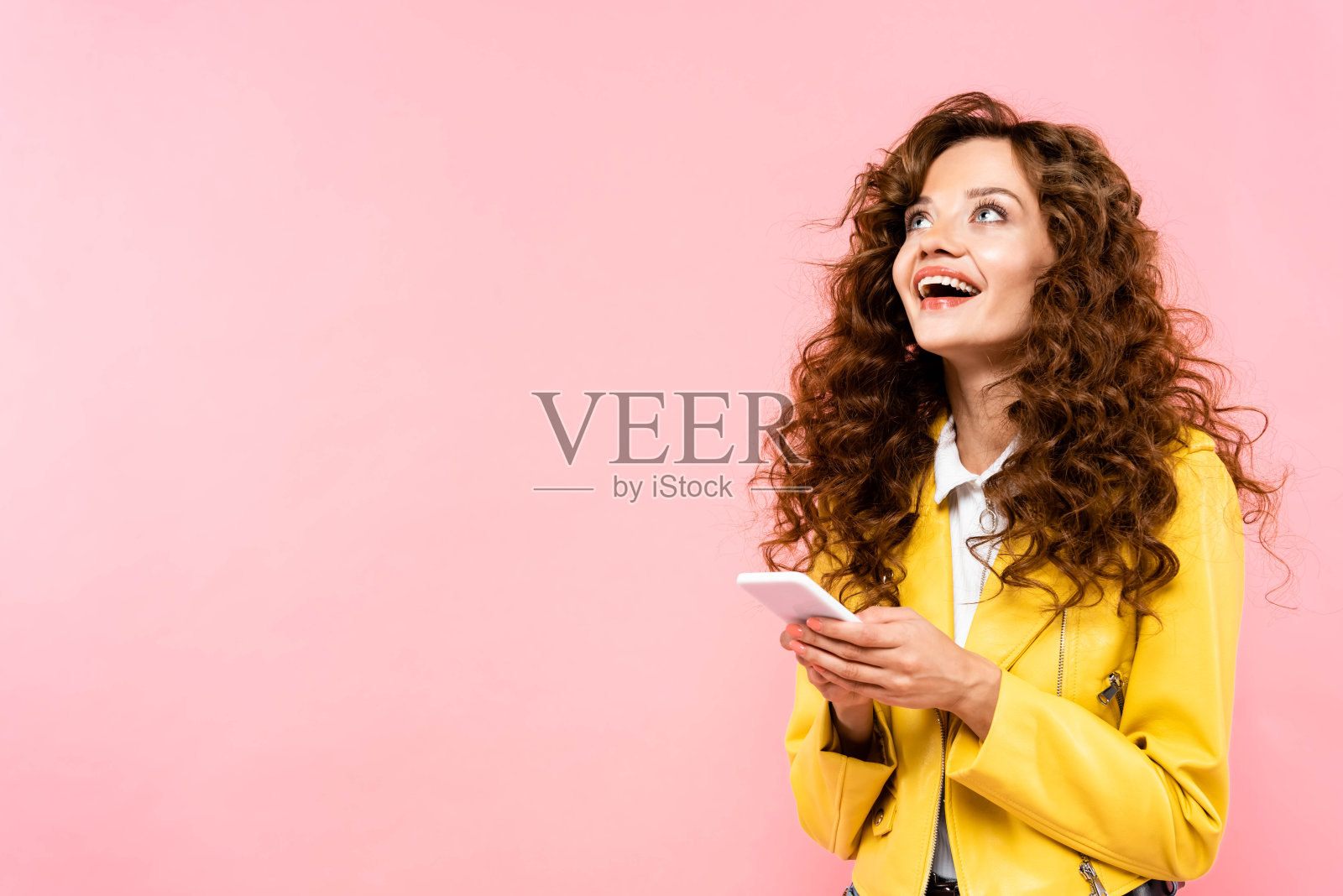 兴奋的卷发女孩使用智能手机，孤立的粉红色照片摄影图片