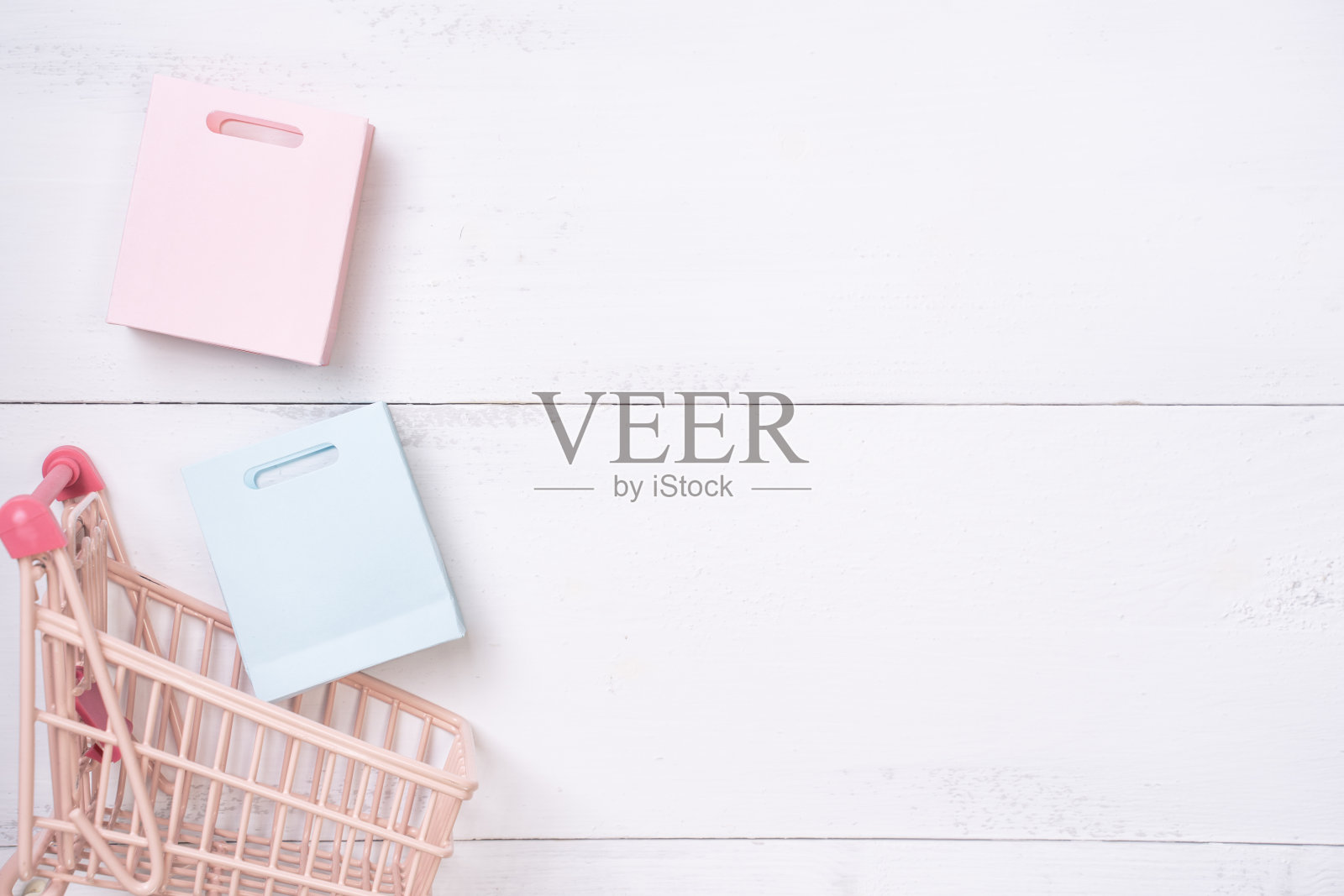 抽象的设计元素，年度销售，购物季节的概念，小手推车与彩色纸袋在白色木制桌子的背景。照片摄影图片